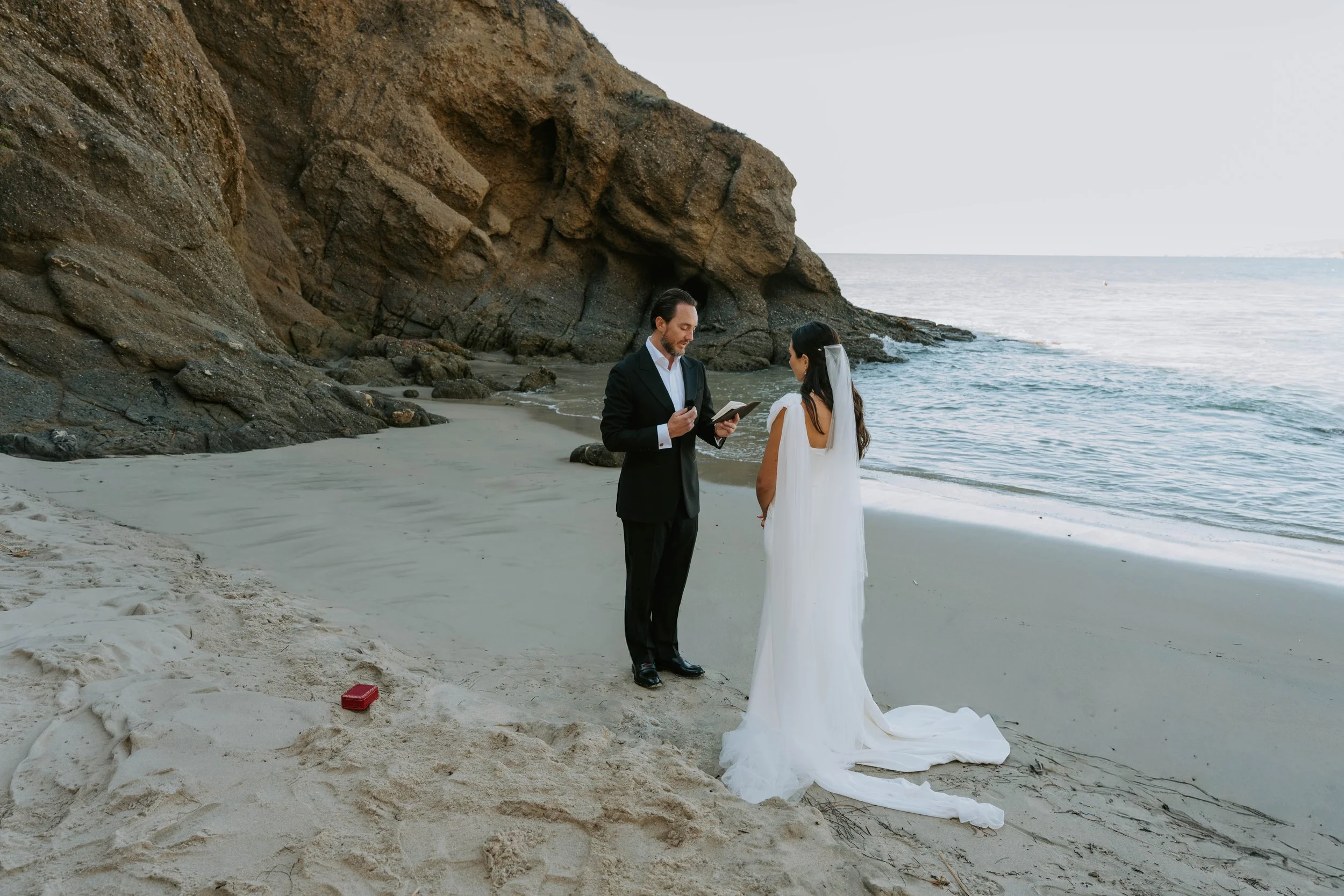 Groom reading his vows as they stand on the beach with the ocean and cliffs in the background