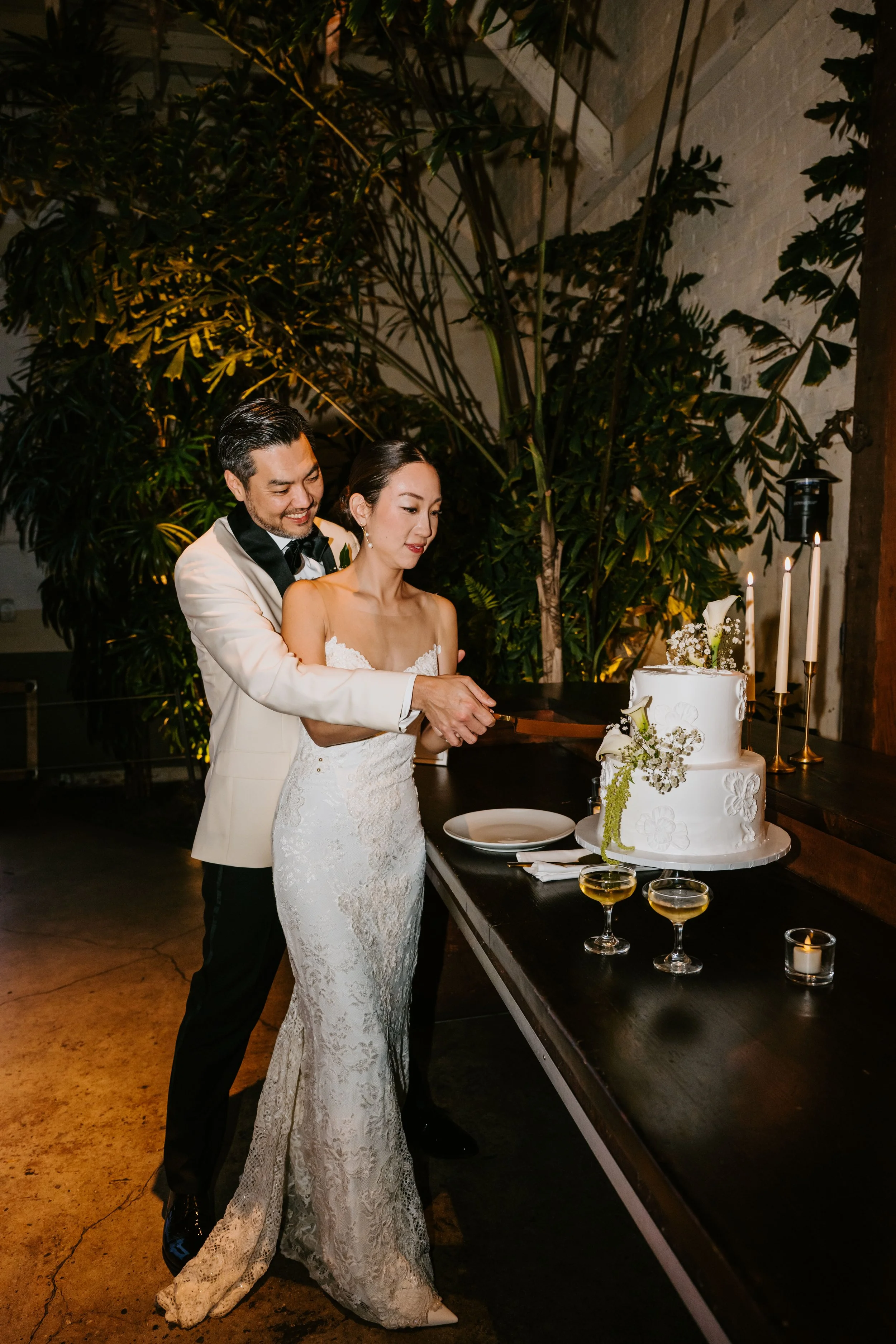 Bride and groom cutting their cake with greenery behind them