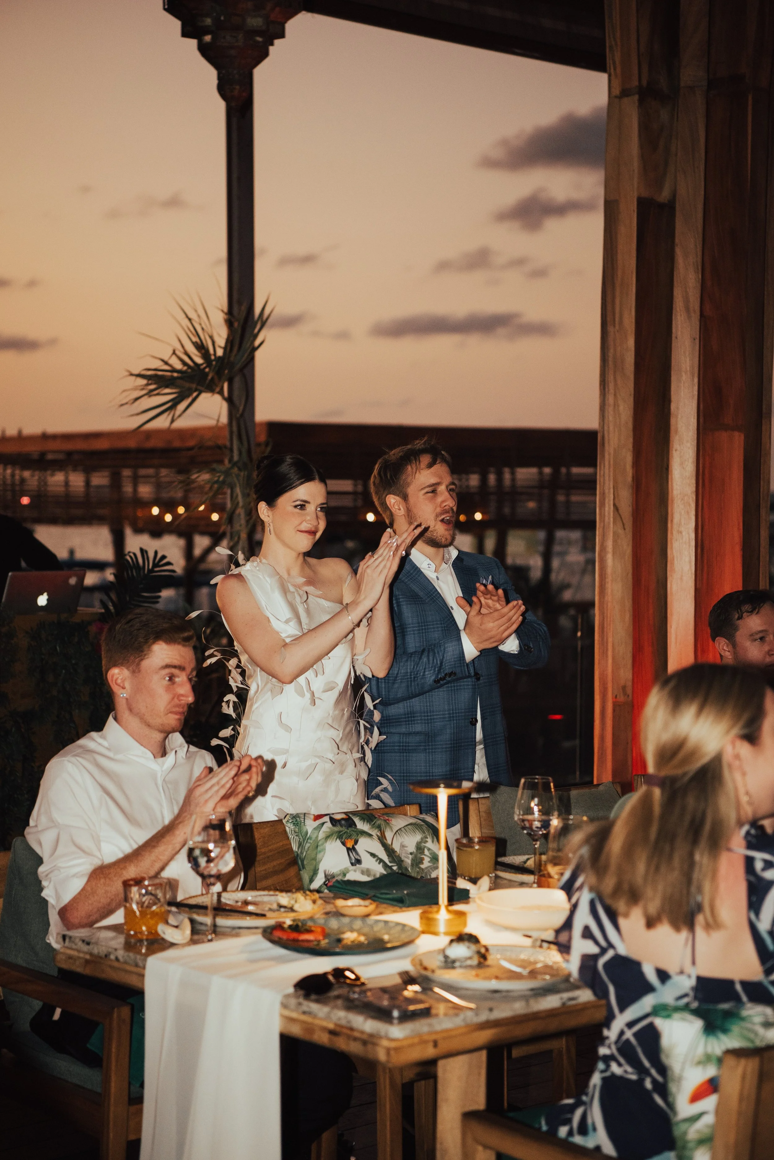 bride and groom clapping and cheering with a pink sunset behind them