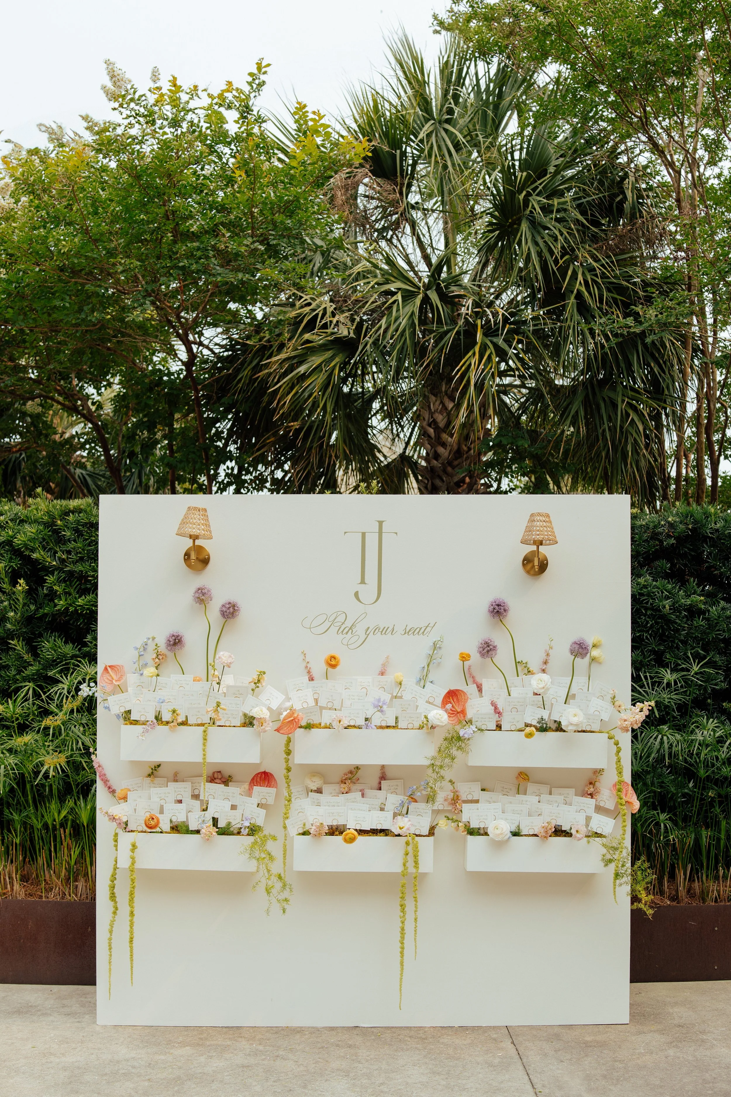 shot of a white wall with shelves containing flowers and place card holders with the wedding guest seat placement.