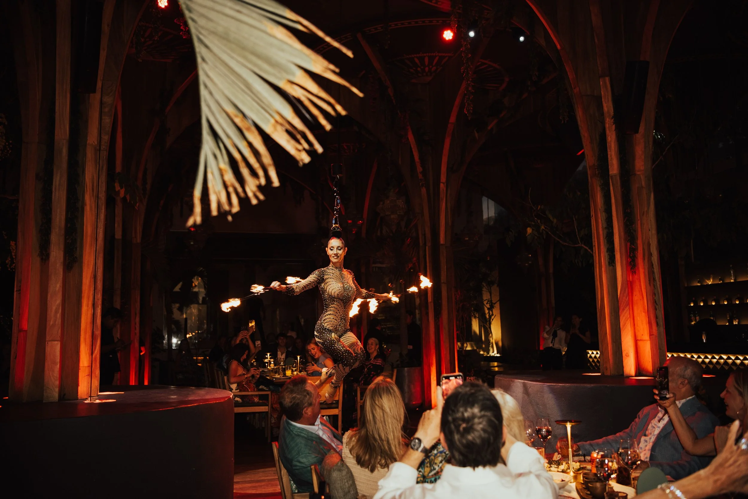 wide shot of arial dance spinning with fire sticks in her hands as guest look on