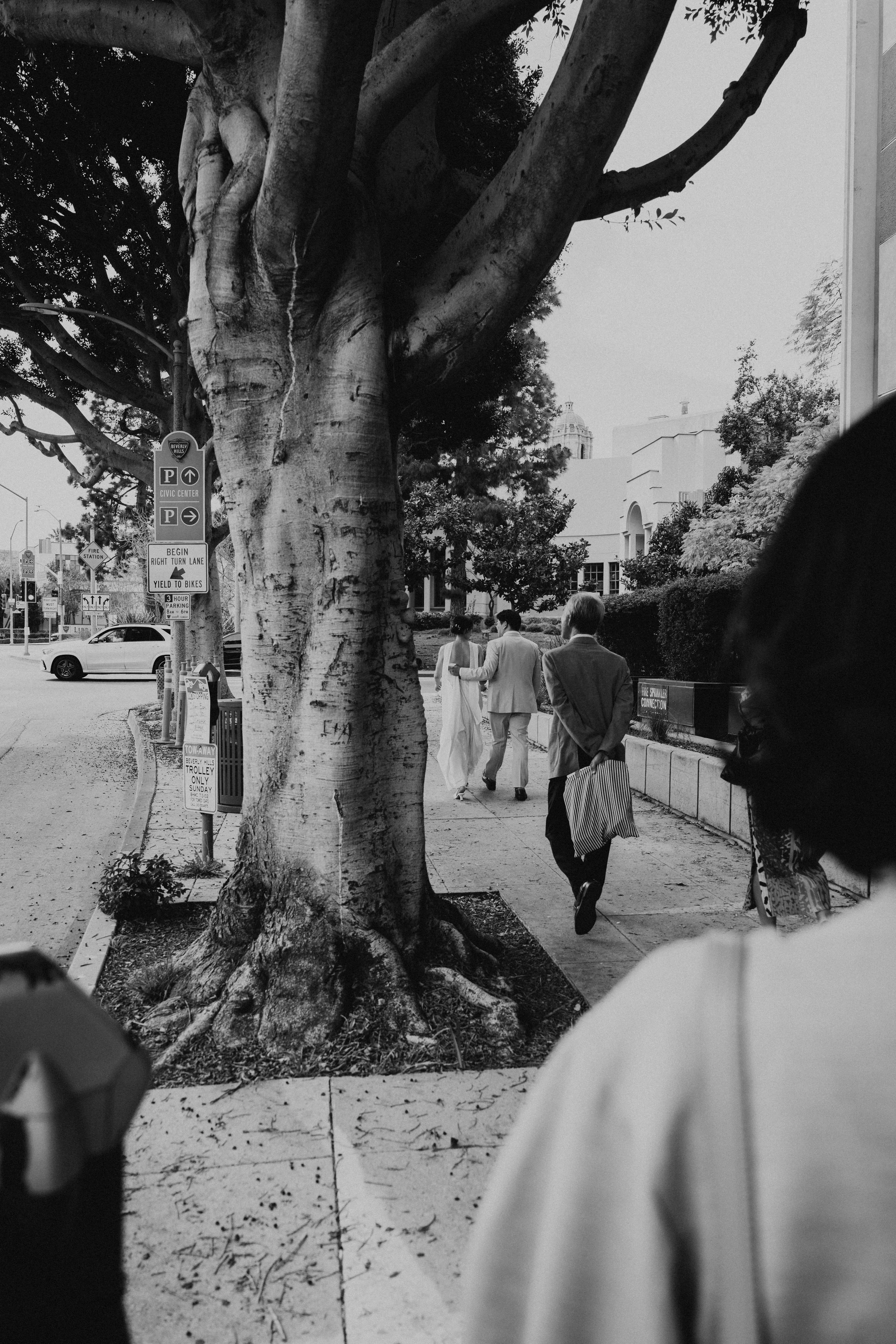 black and white photo of bride and groom walking with family down the sidewalk after wedding ceremony
