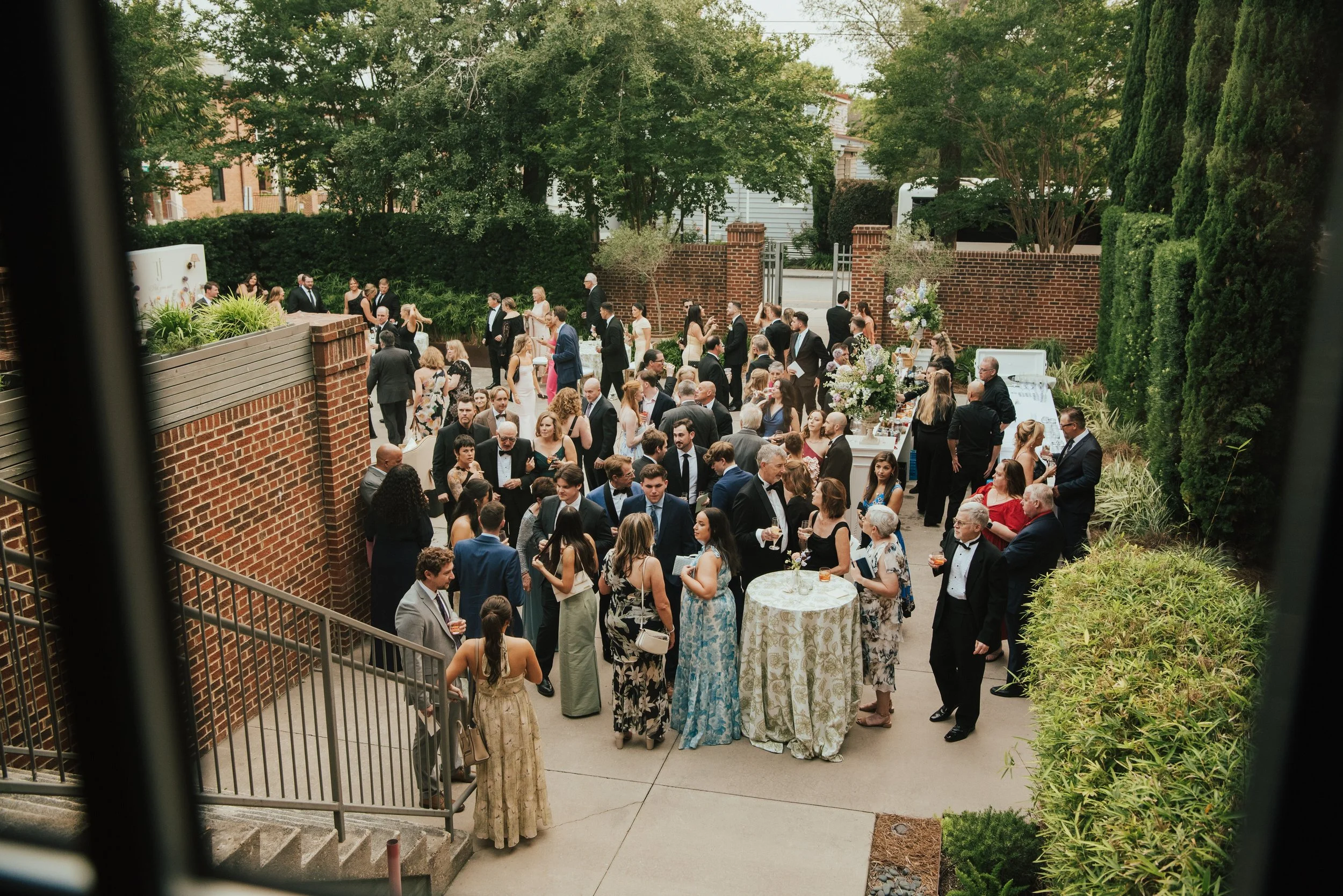 wide shot of wedding guest mingling at cocktail hour. Shot through a window looking down on the party