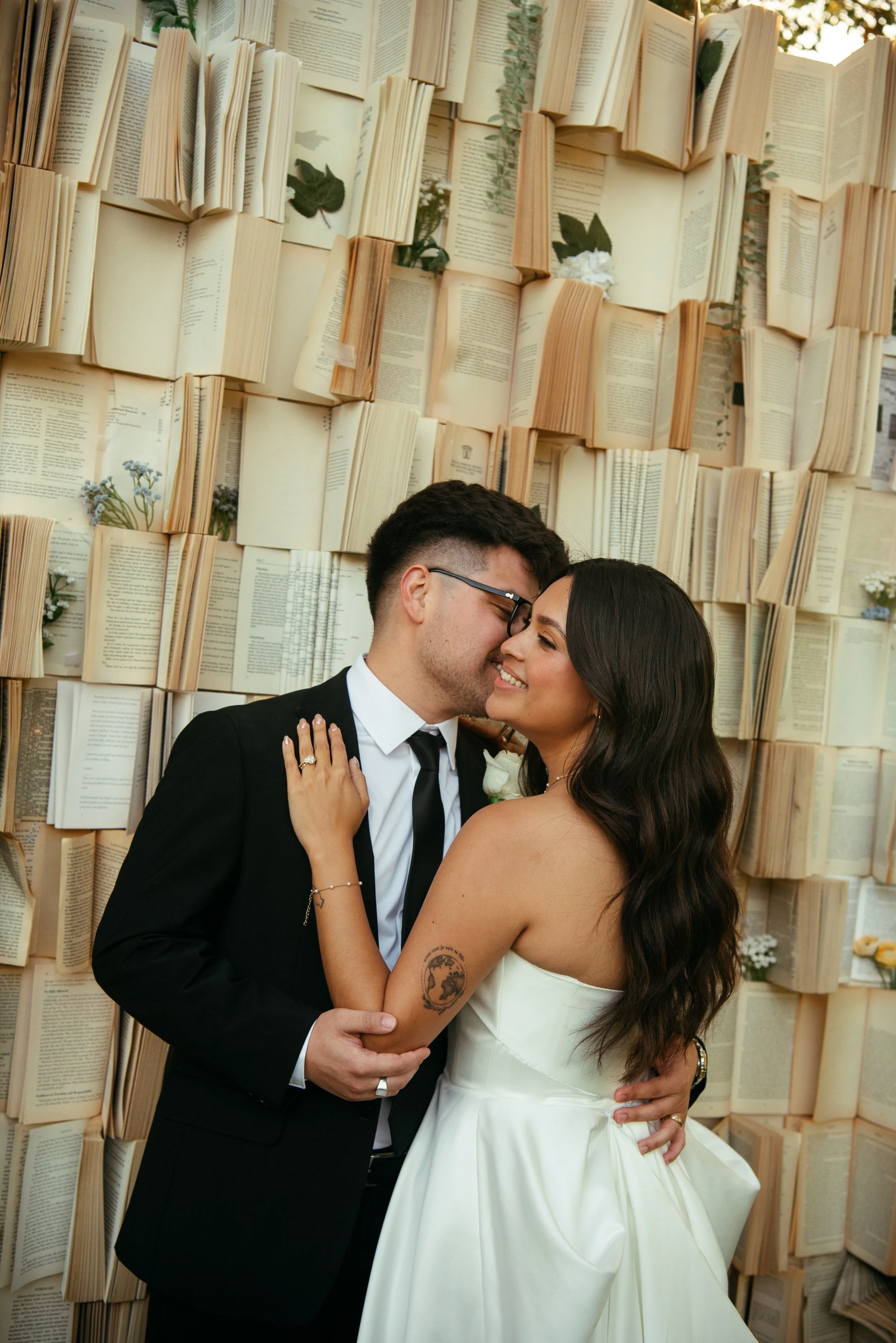Groom kissing brides cheek in from of book wall.