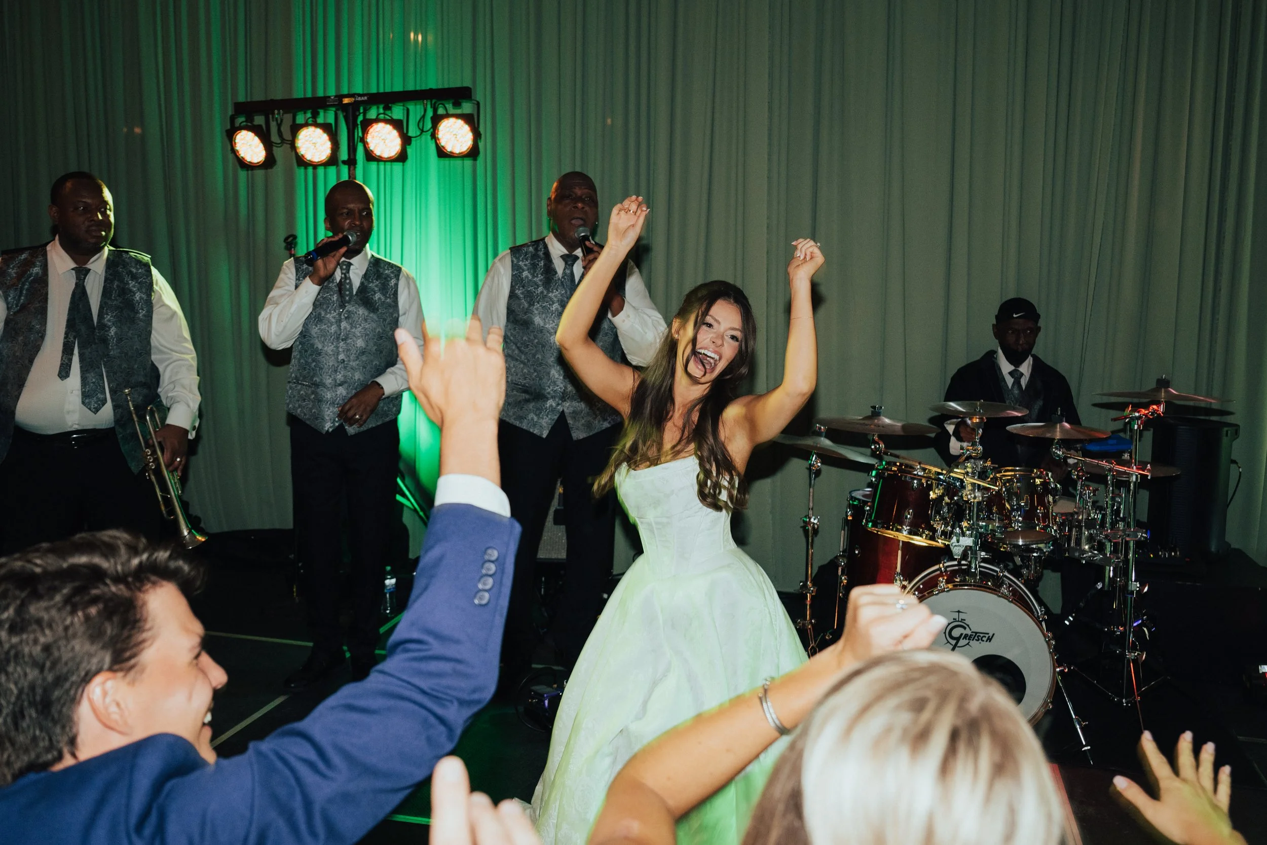 Bride dancing on stage with the live ban behind her as guest cheer her on
