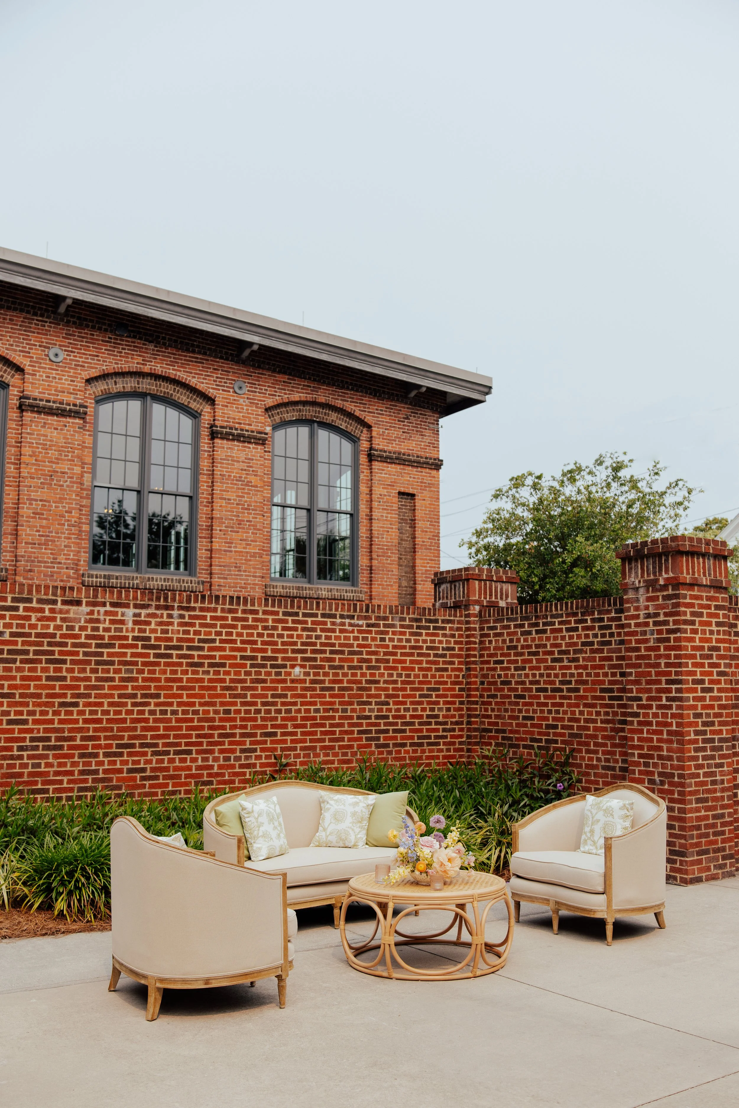 chair and couch set up for cocktail hour with pastel floral arrangement in from brick builing