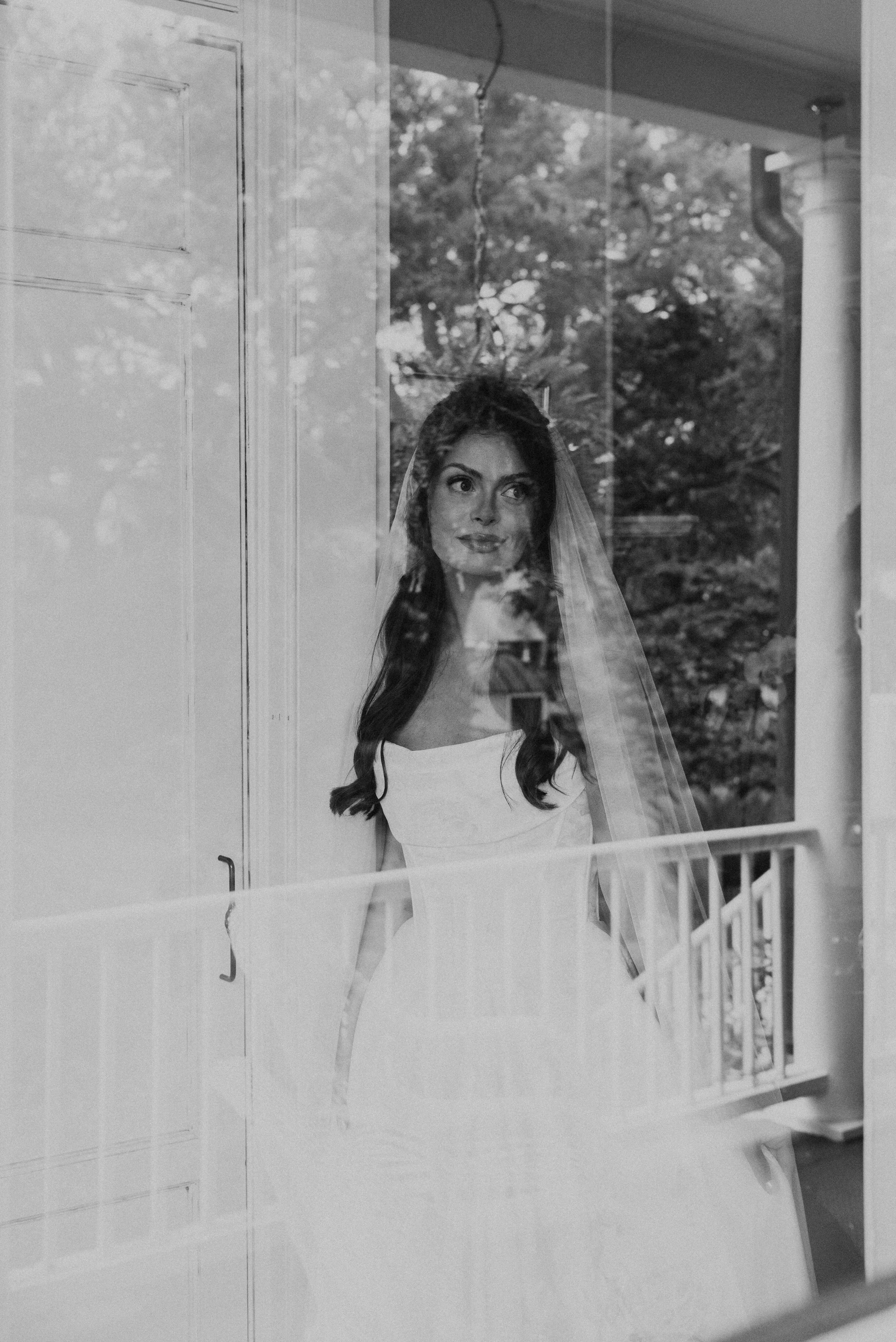 Black and white photo of a bride on her wedding day shot through a window