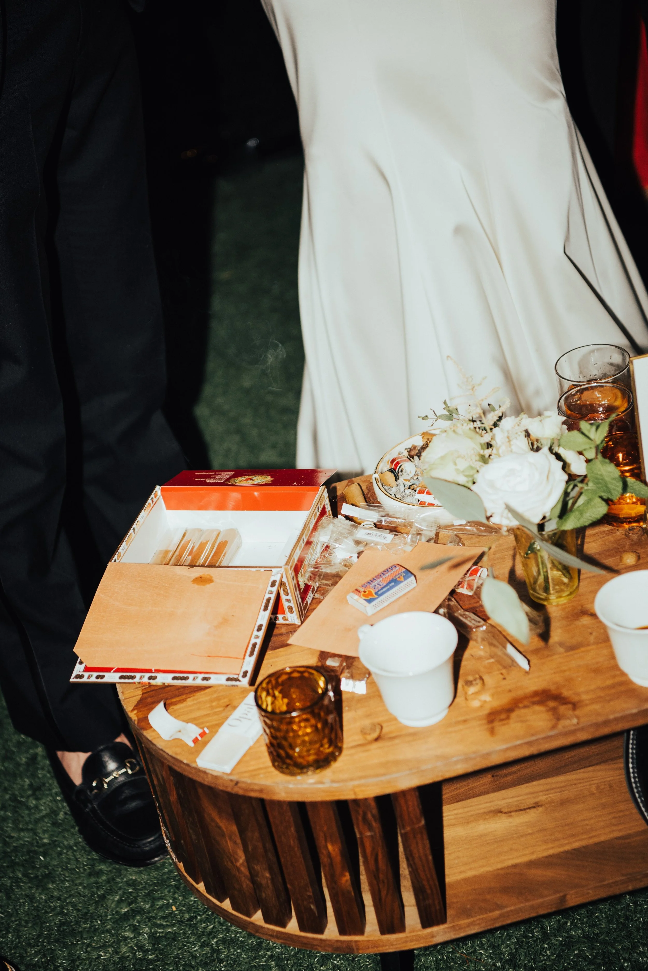 close up shot of wooden table covered in cigar wrappers, box of mostly empty cigar box, and drinks.