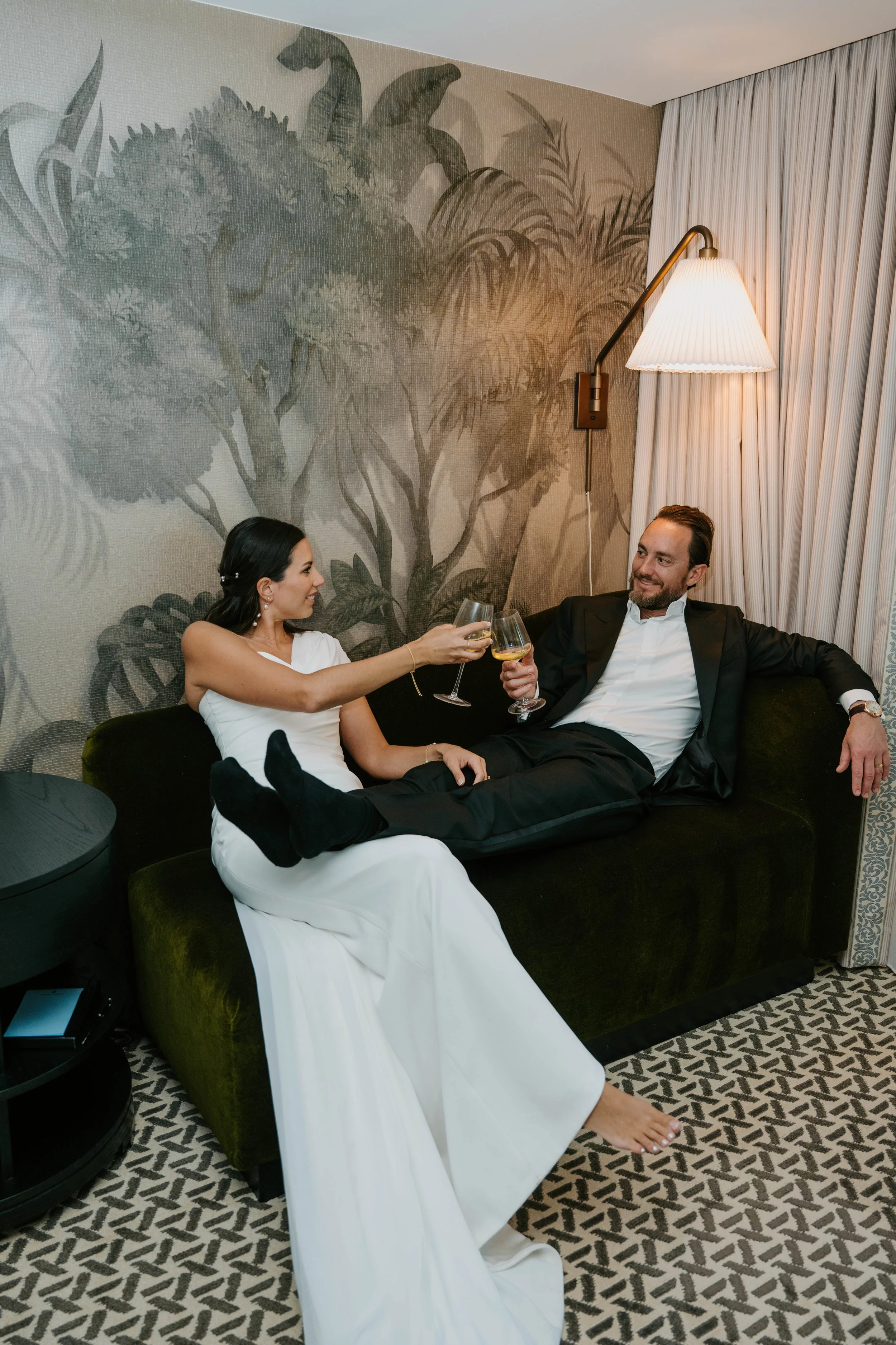 Bride and groom sitting on couch cheers with Champagne