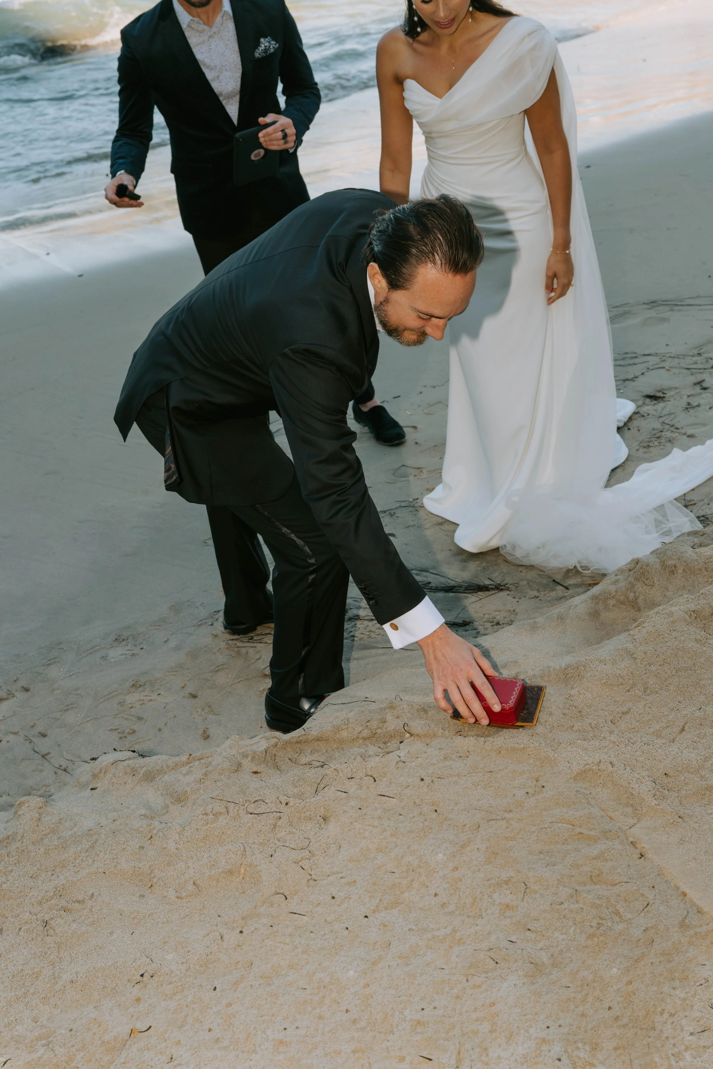 groom picking up ring box out of the sand during their ceremony