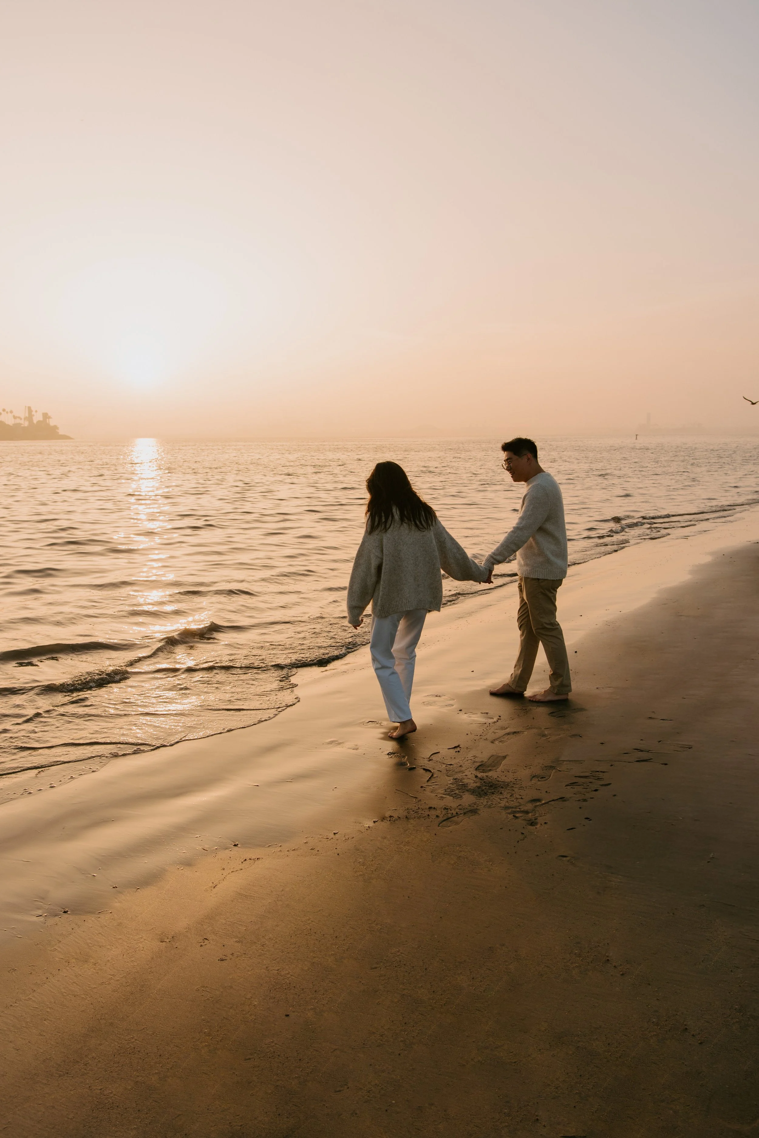 Couple walking toward the water holding hands as the sunset over the water