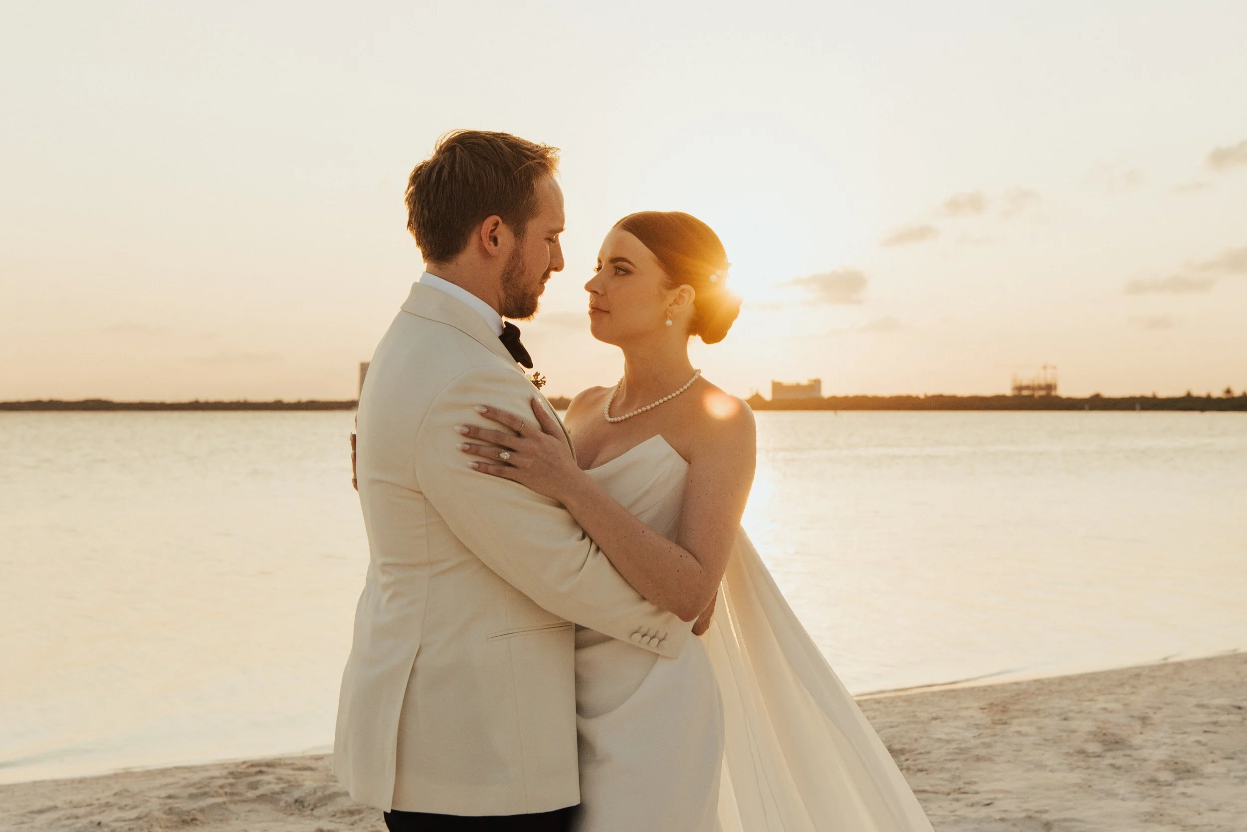 bride and groom embracing on the beach with sun setting behind them
