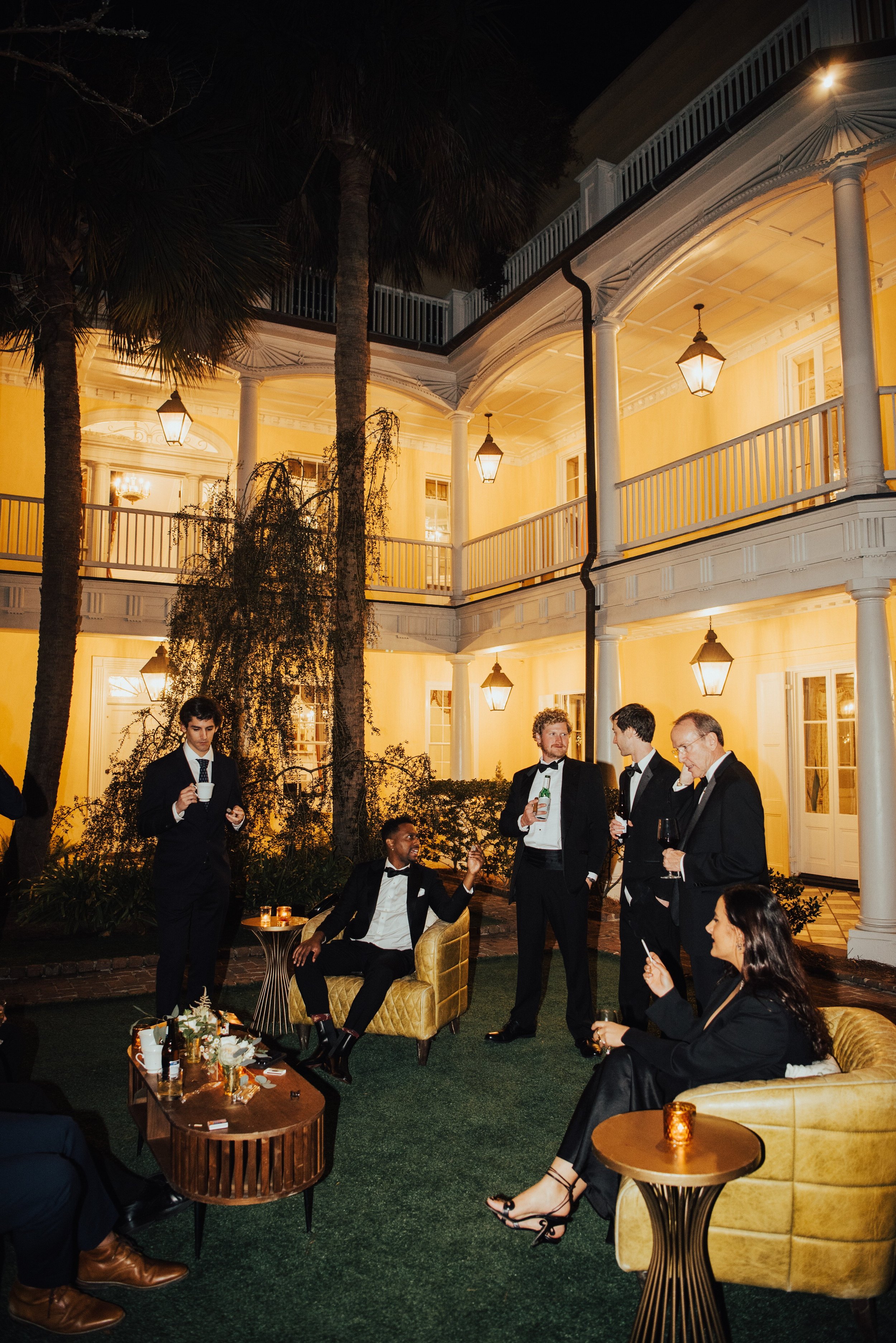 Wedding guest hanging around on the lawn at night smoking with the two story yellow house in the background