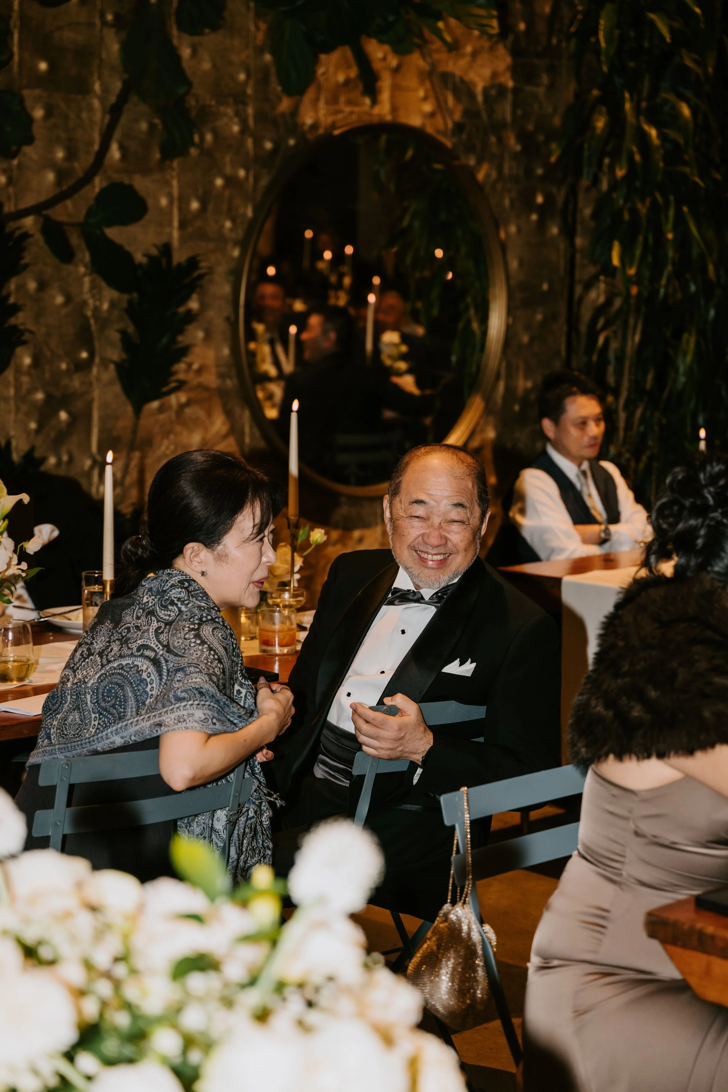 Bride's grandfather sitting in a chair turn sideways in it smiling at the camera