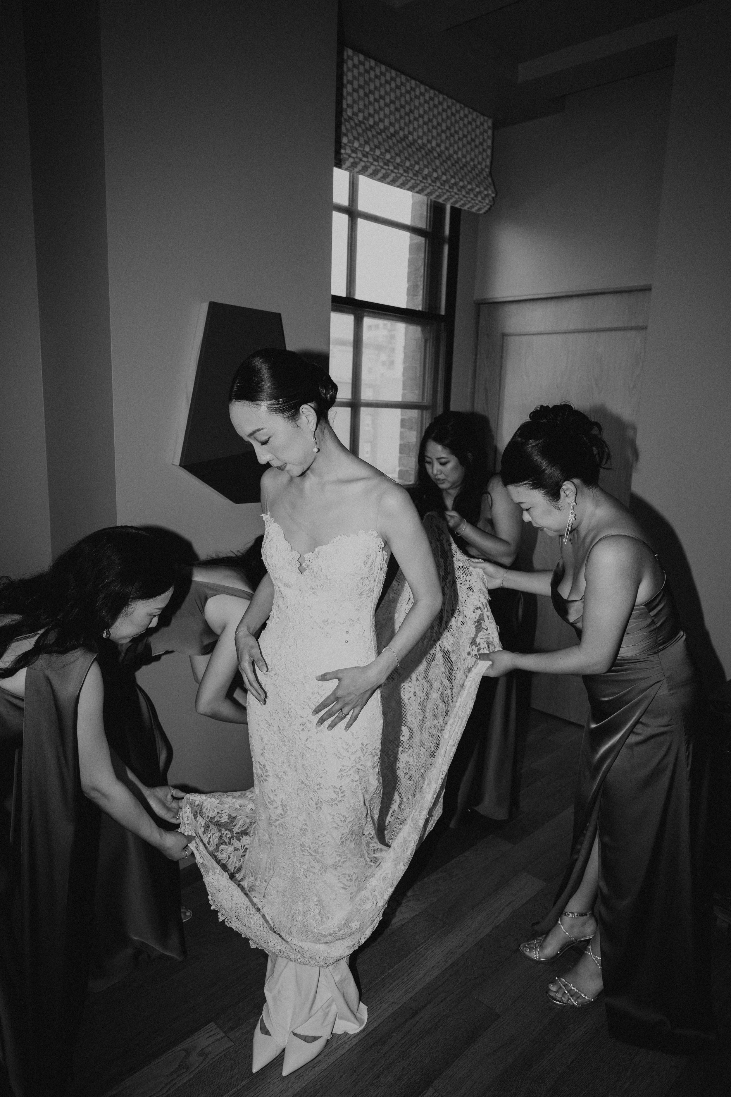 Black and white photo of Bridesmaid fluffing brides dress