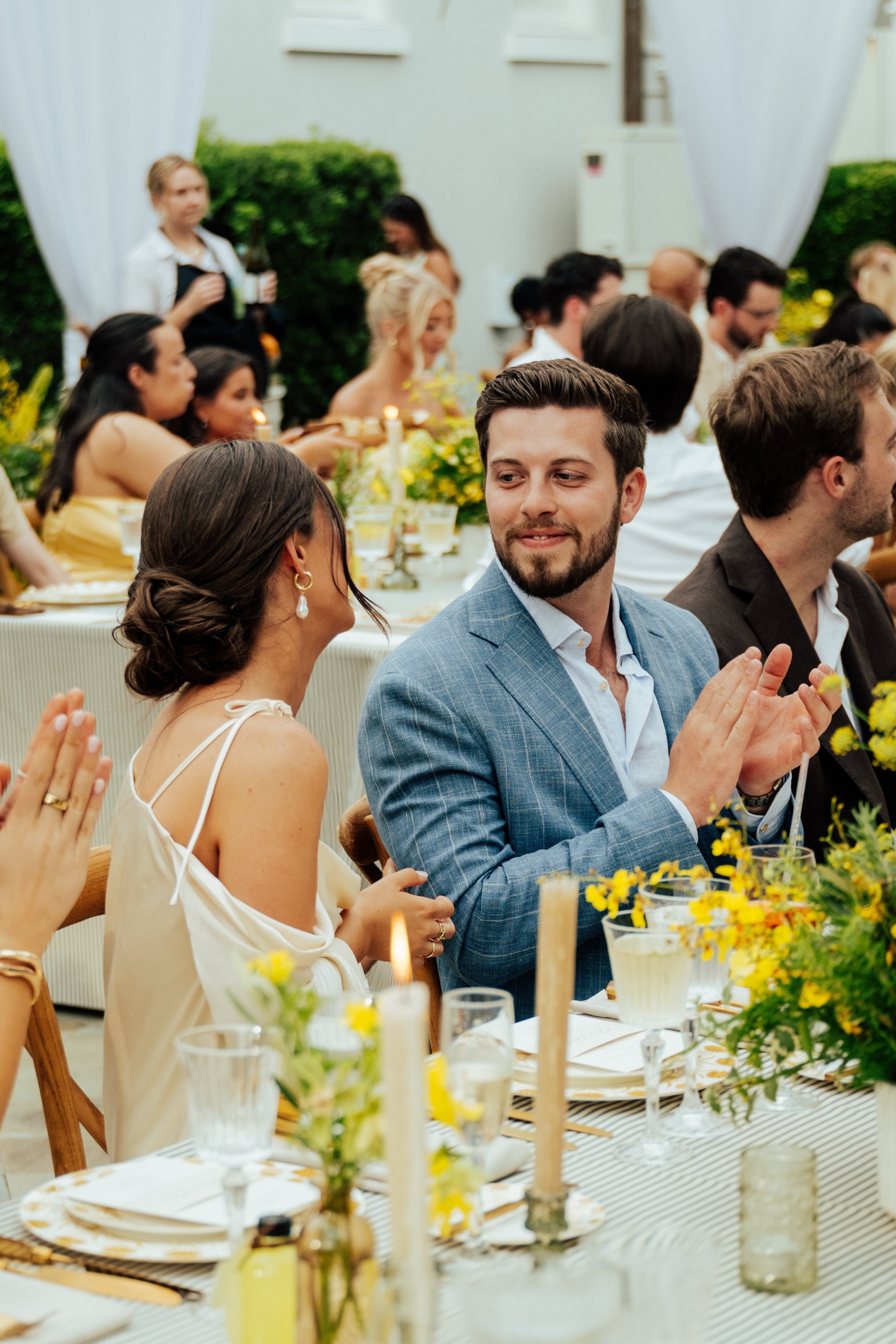 man in blue suit looks lovingly at woman in white dress as they sit at a table