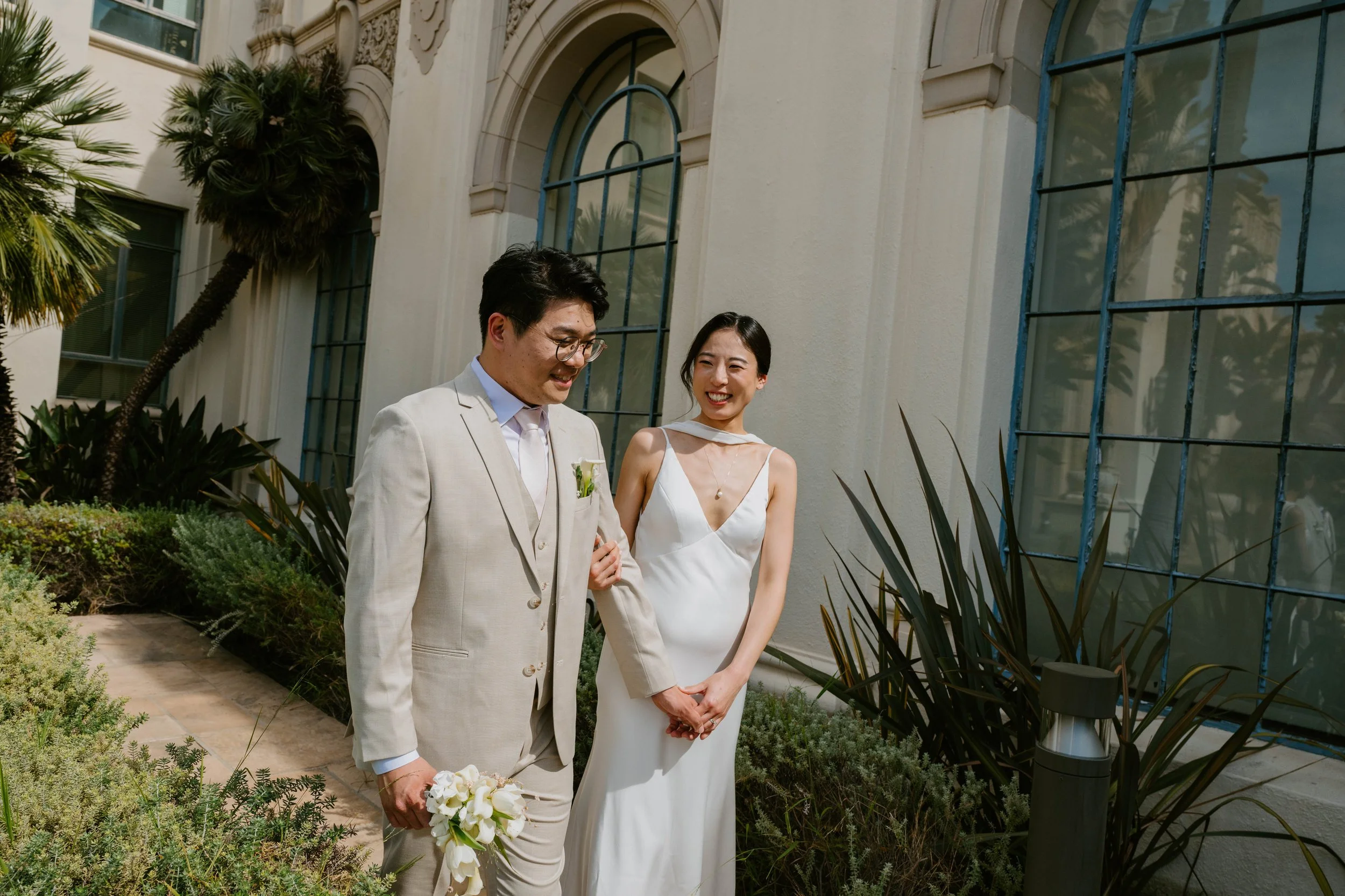 Bride and Groom walking in front of the arched windows of the Beverly Hills City Hall