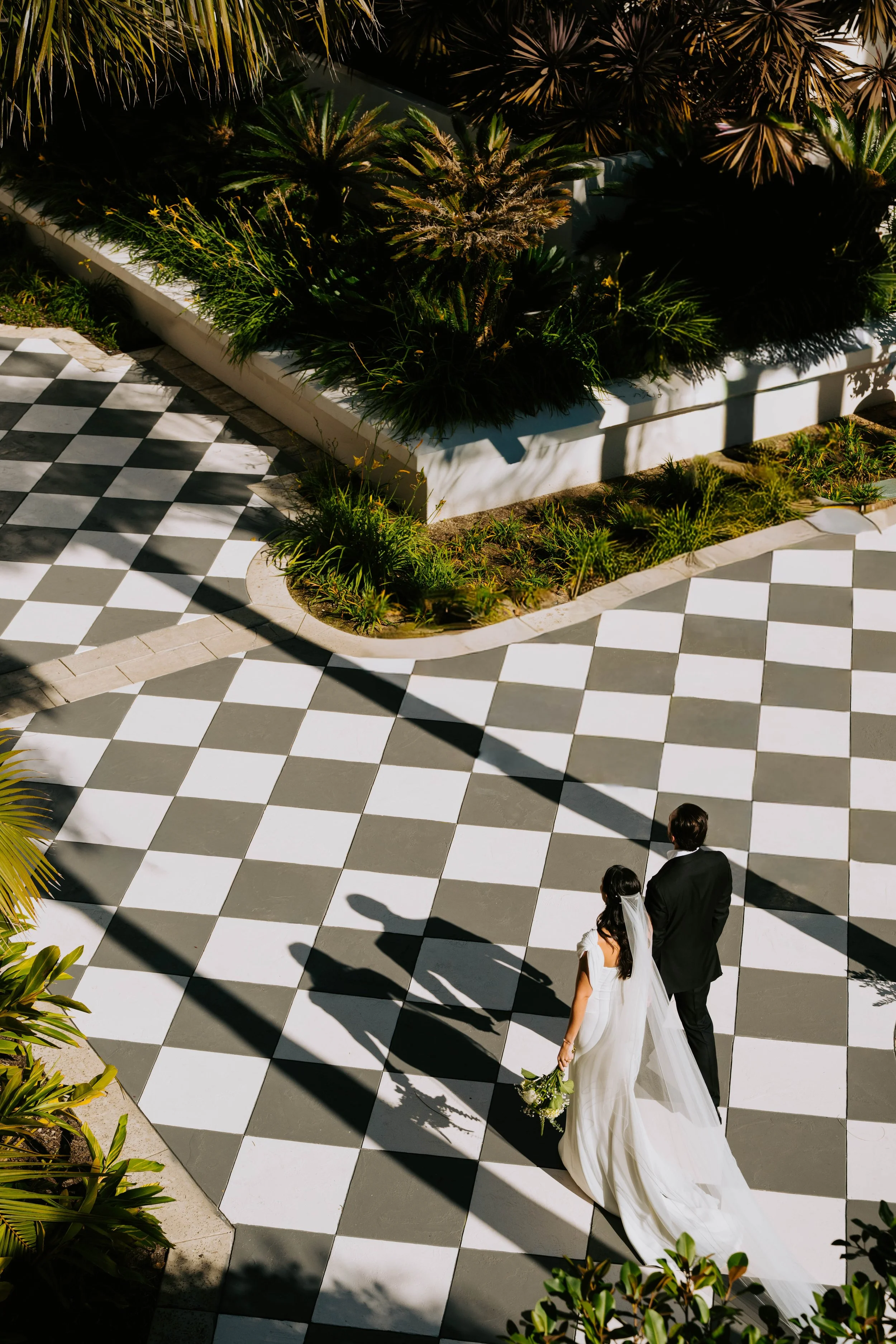 Photo shot from above. Bride and groom walking away from the camera on a checkered floor. You can see their silhouette shadows in front of them