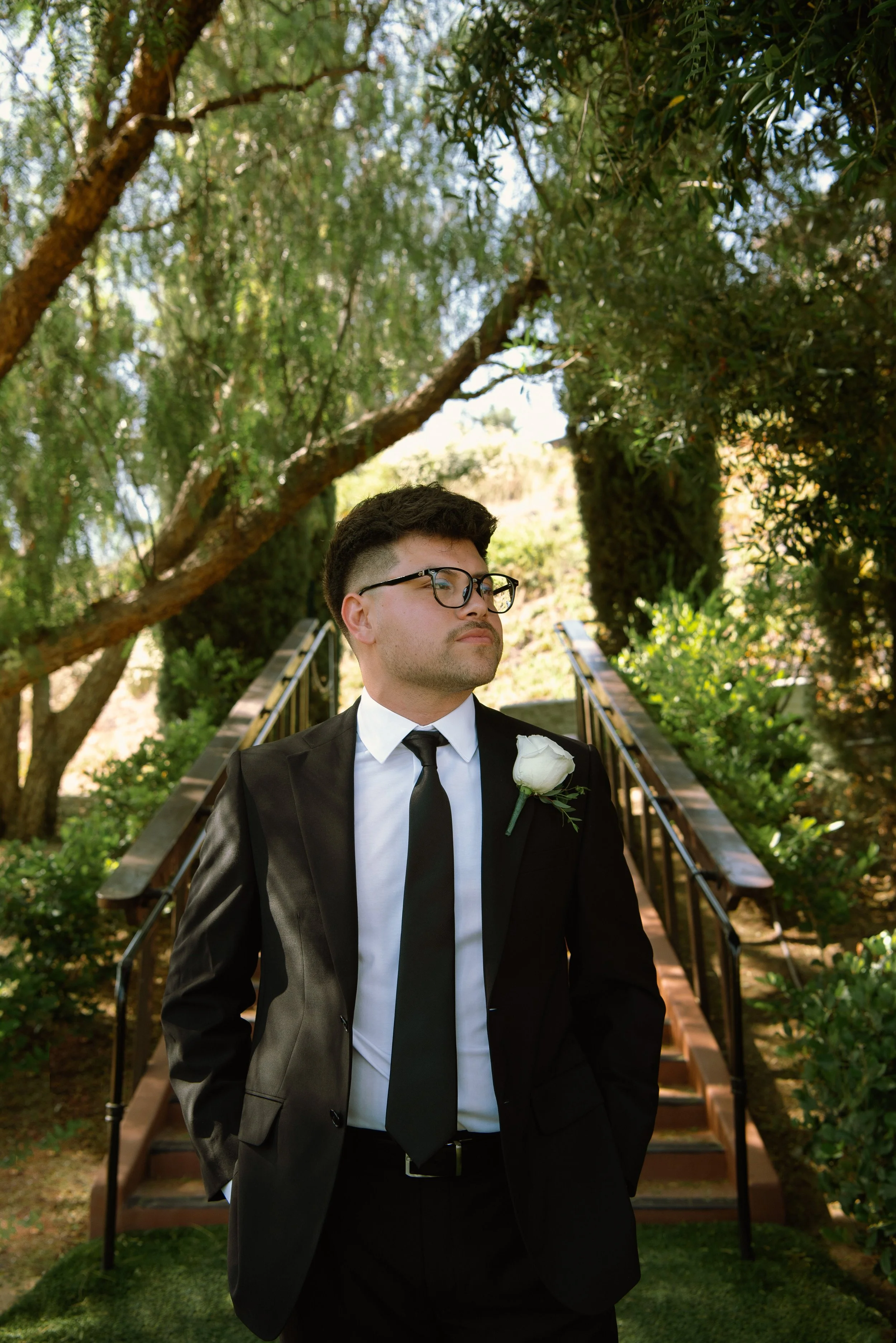 Close up shot of Groom under some tress, He is look off to the side