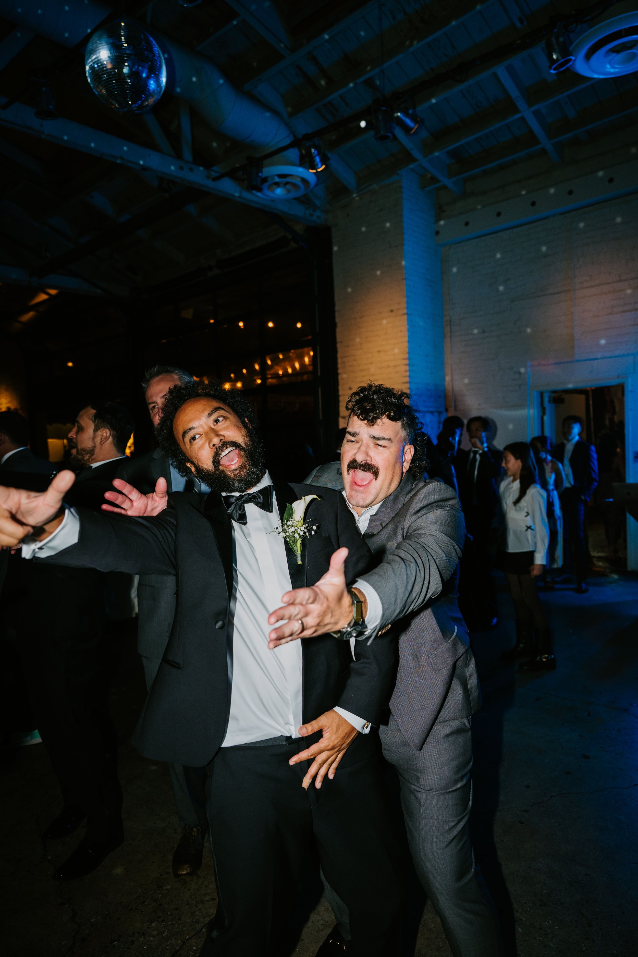 two wedding guest dancing and reaching for someone off camera