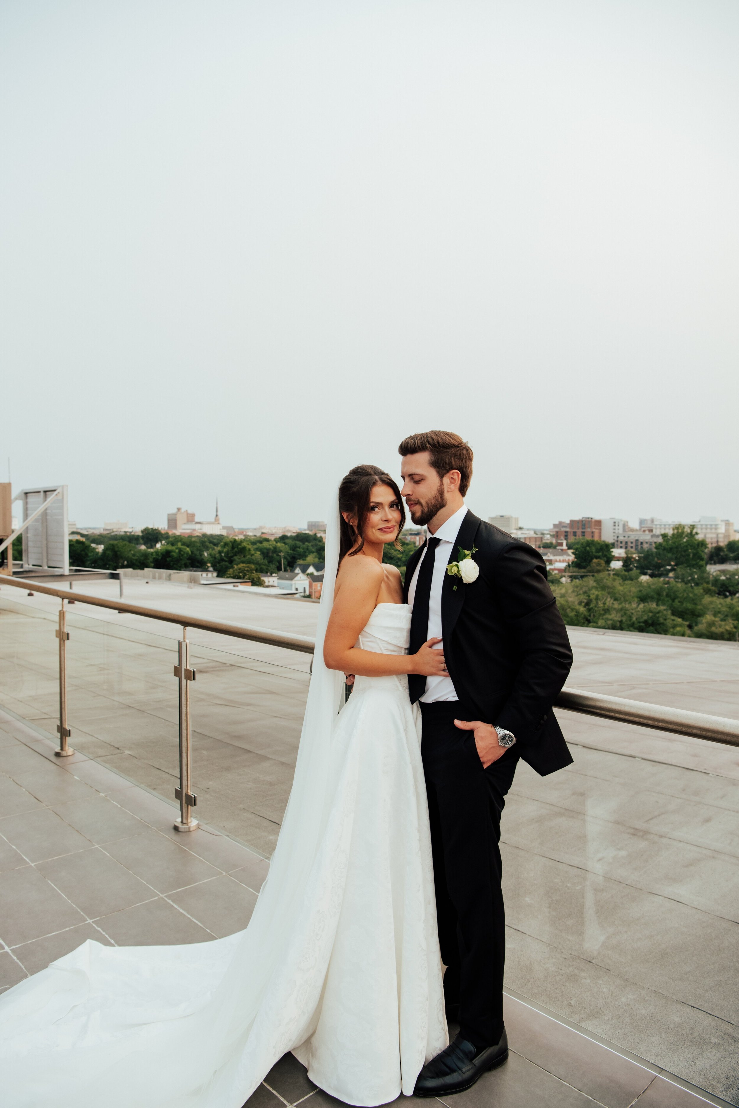 Shot of bride and groom on a roof top. Bride is looking at the camera as the groom looks down at the bride