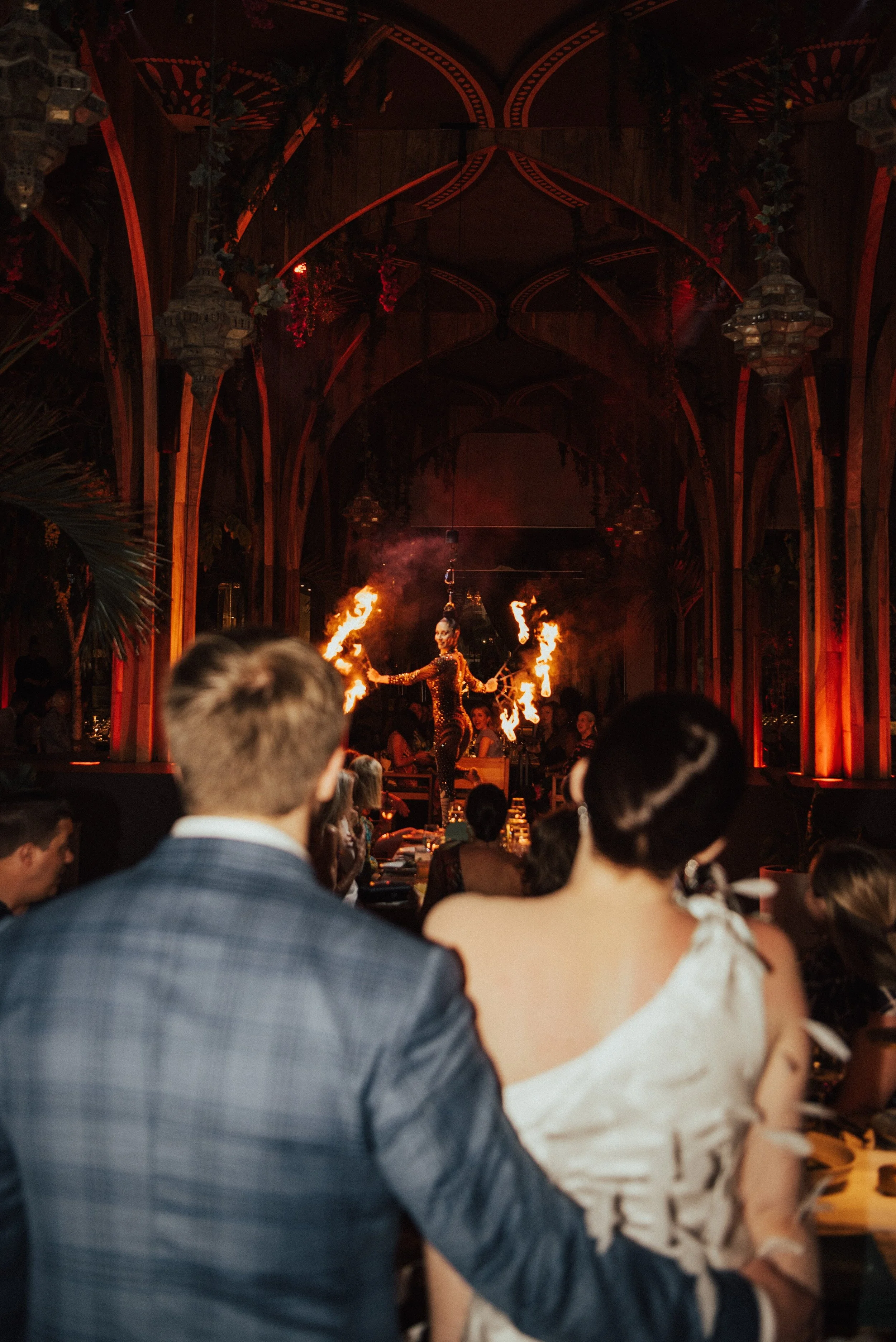 photo shot over bride and grooms shoulders as an arial dancers spins in the air with firs sticks