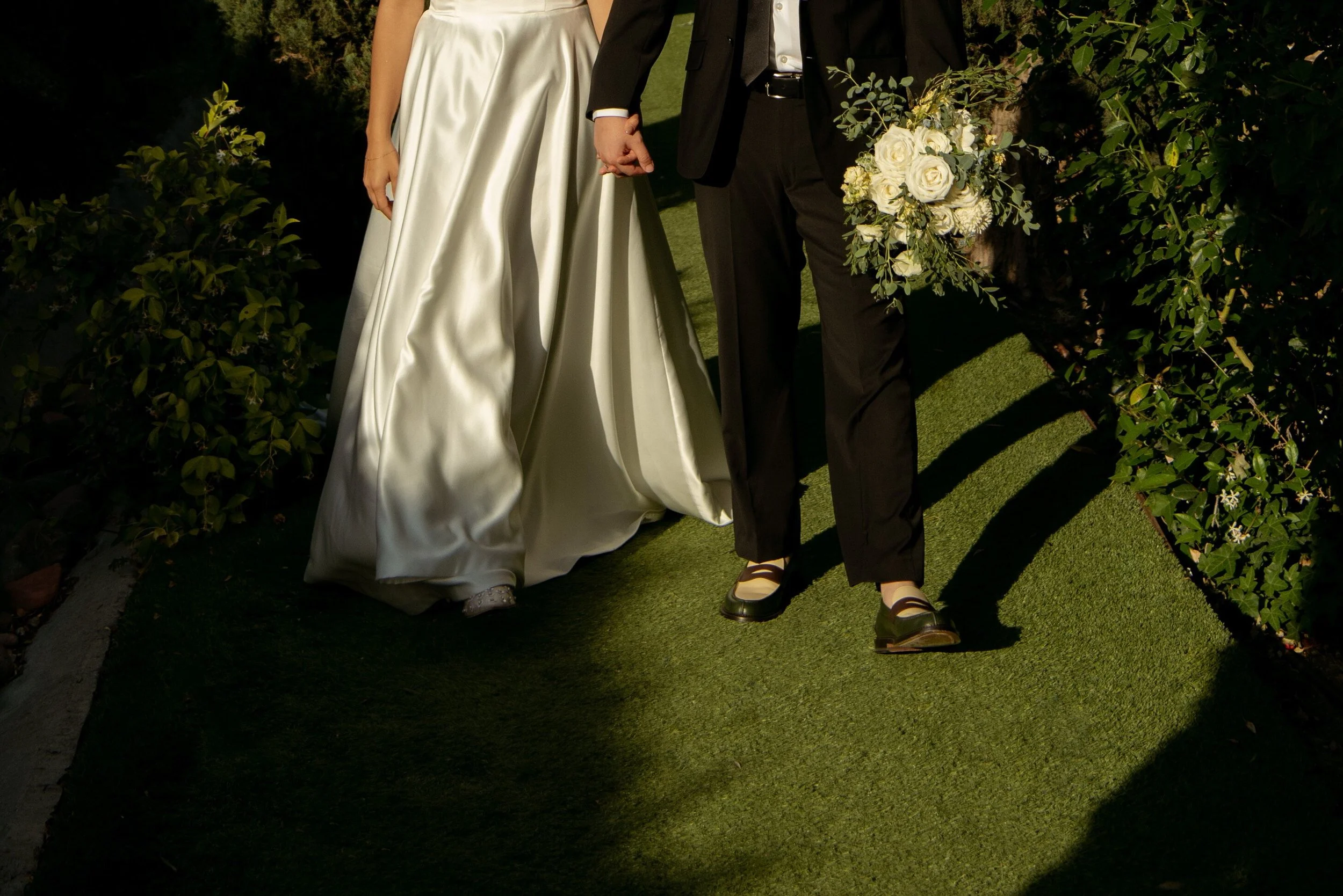 Close up of bride and groom walking from waste down. You can see they are holding hands and groom is holding bouquet