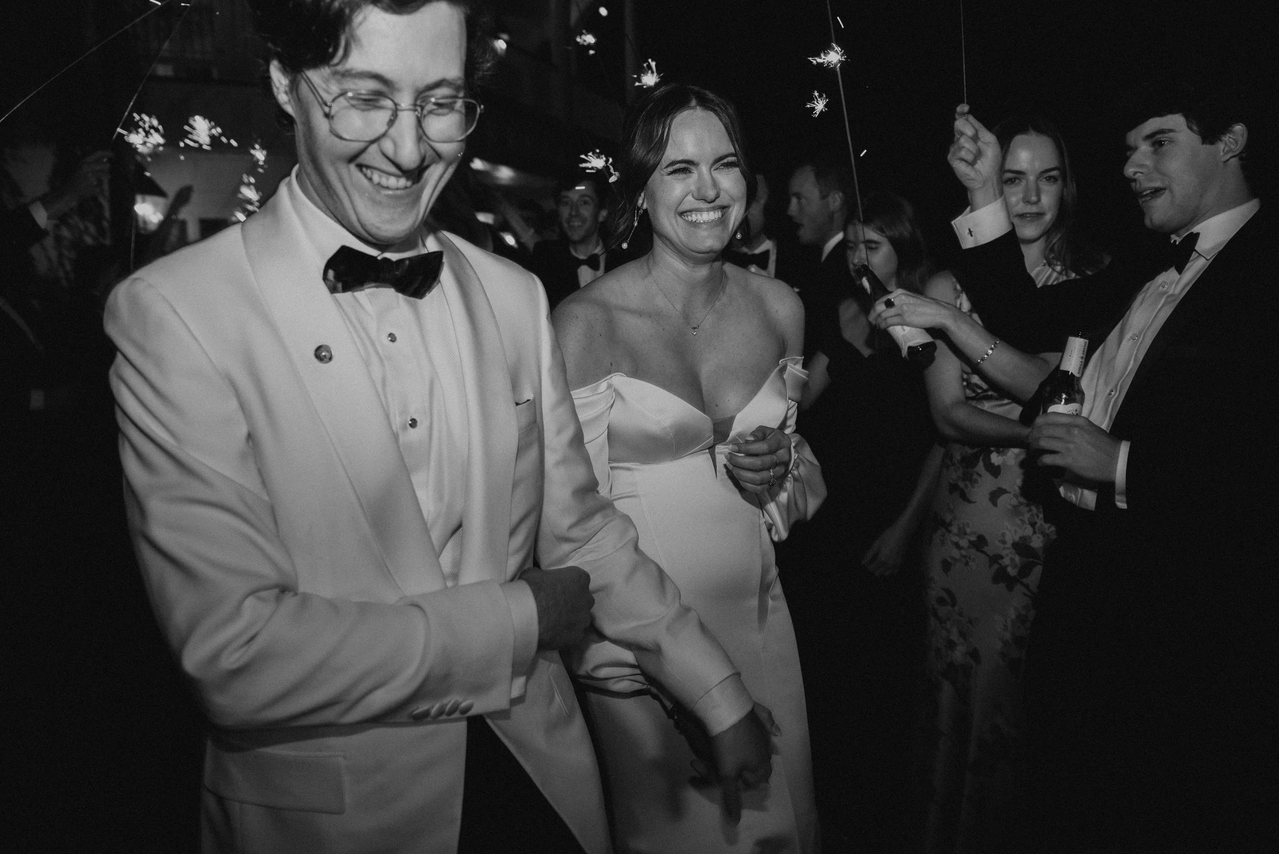 Black and white photo of bride and groom running through the sparkler exit.