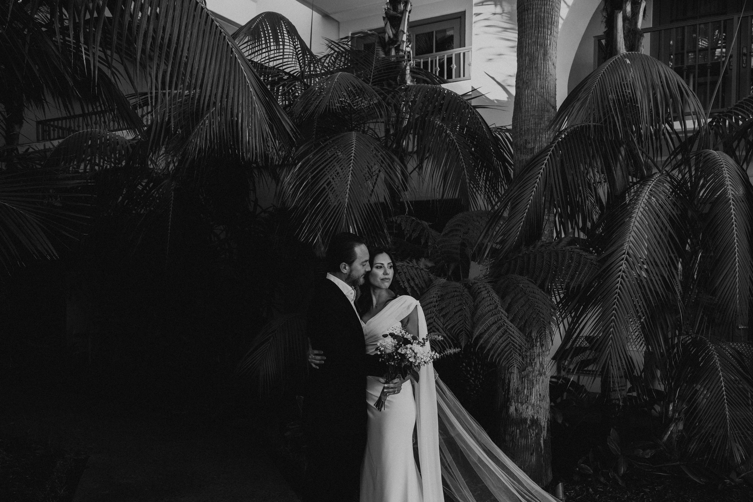 Black and White photo of Bride and groom hugging in from of trees. Bride is looking off to the side.