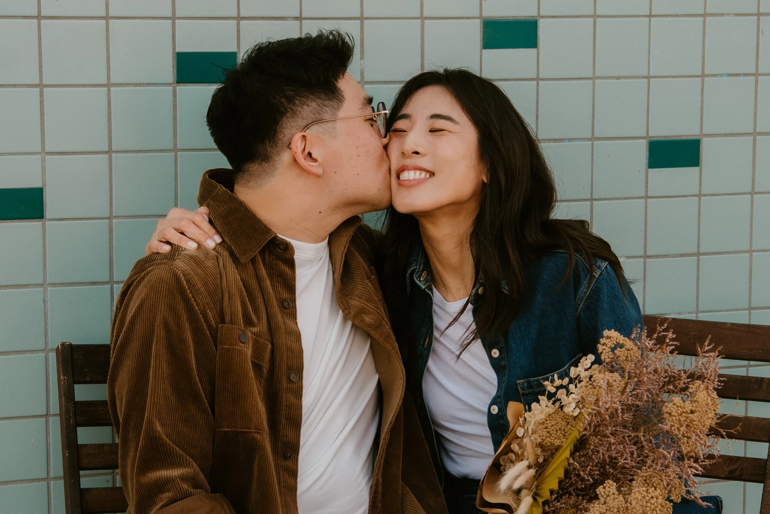 close up photo of guys kissing girl on the cheek. She is smiling