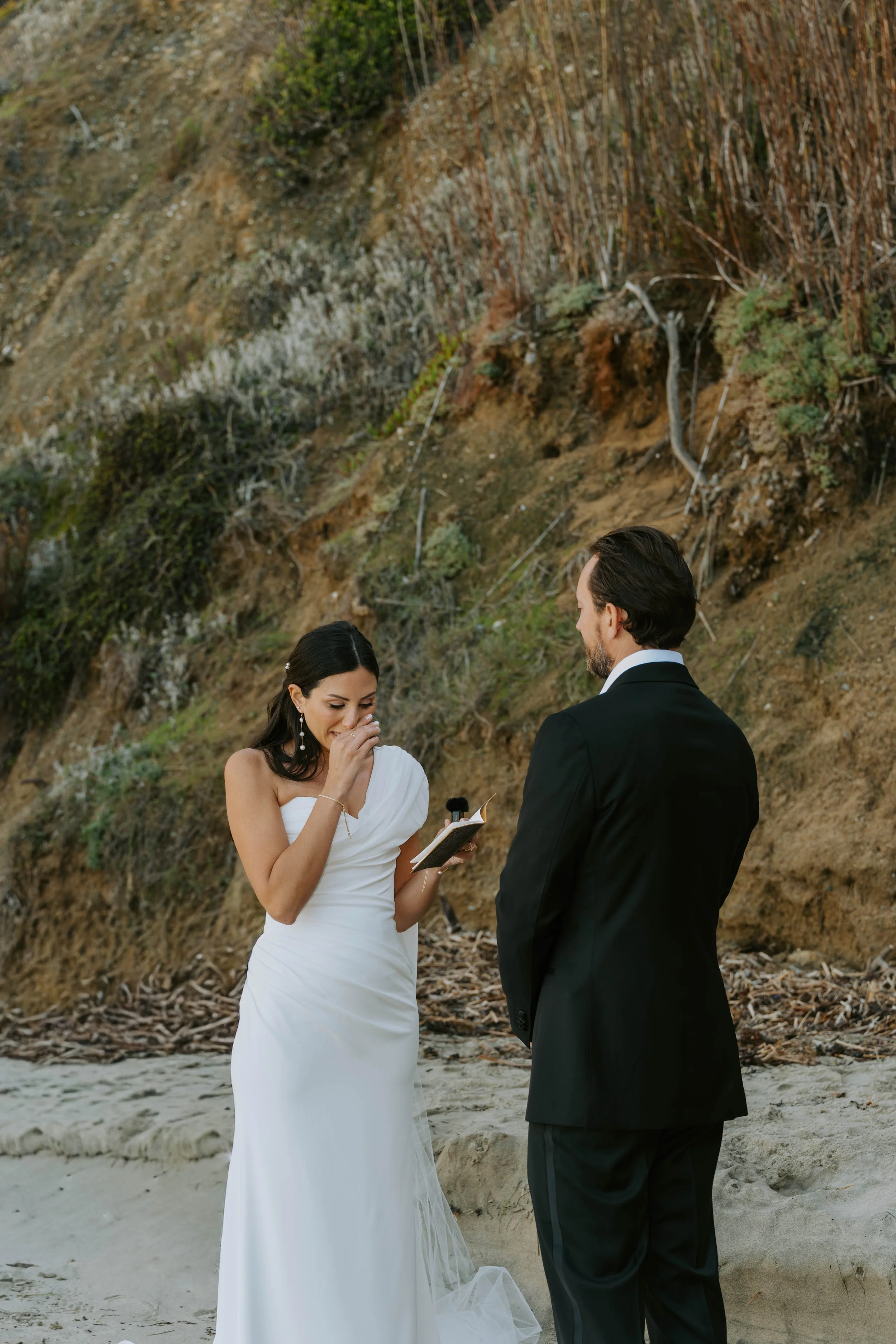 Bride wiping tears away as she reads her vows to her groom