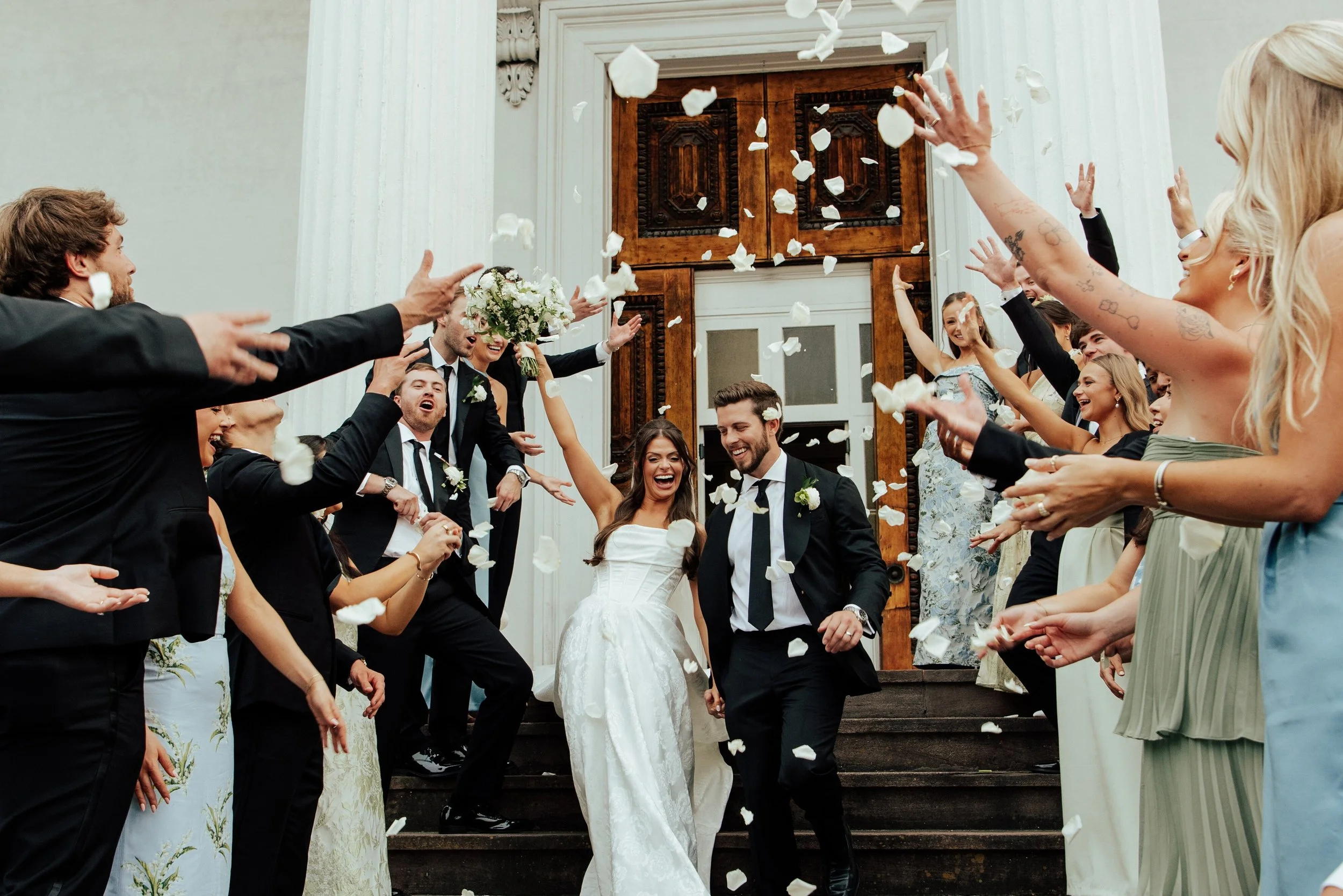 Bride and Groom walking down the steps of a church as their friend and family throw flower petals in the air