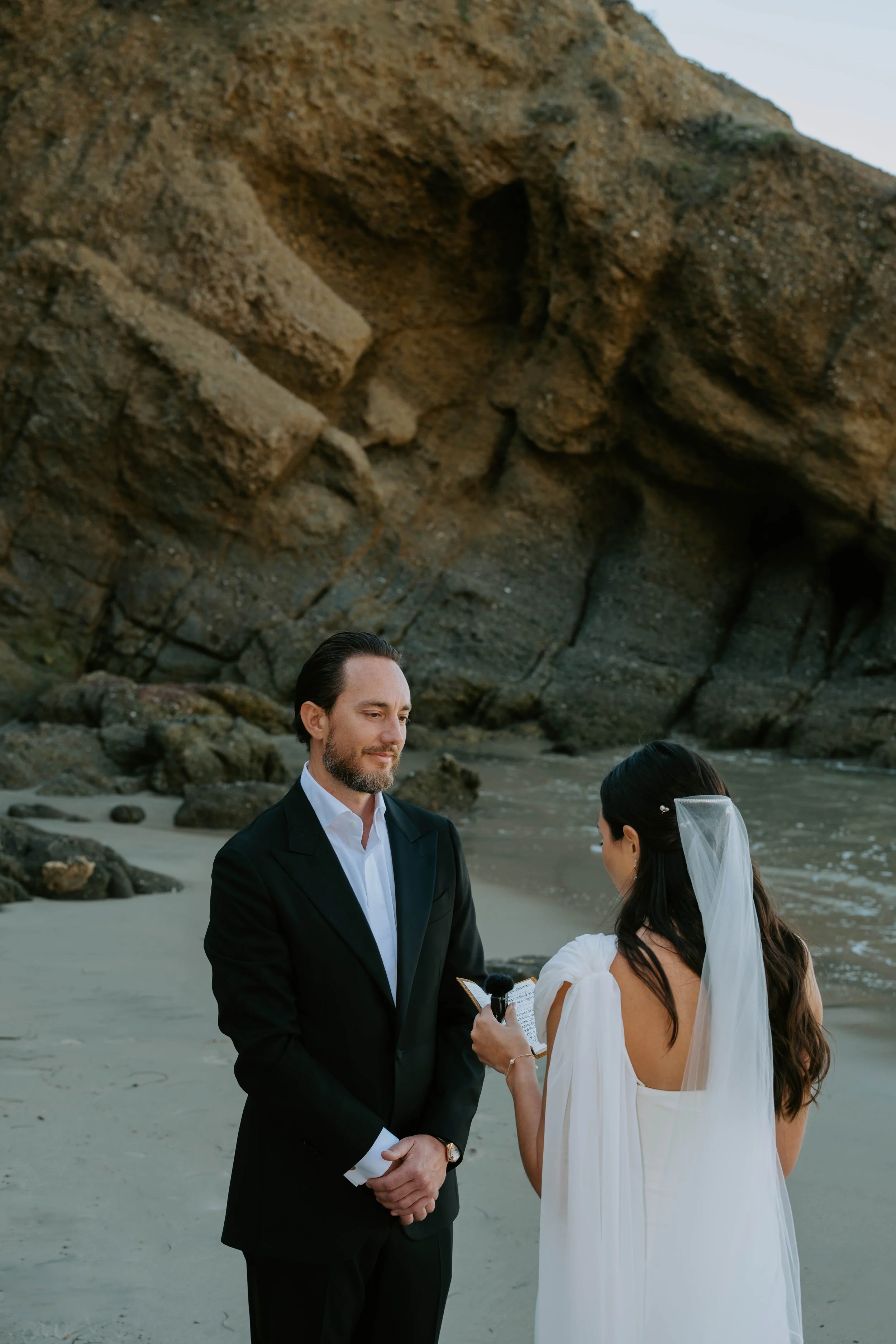 Groom looking at bride as she reads her vows with cliffs in the background