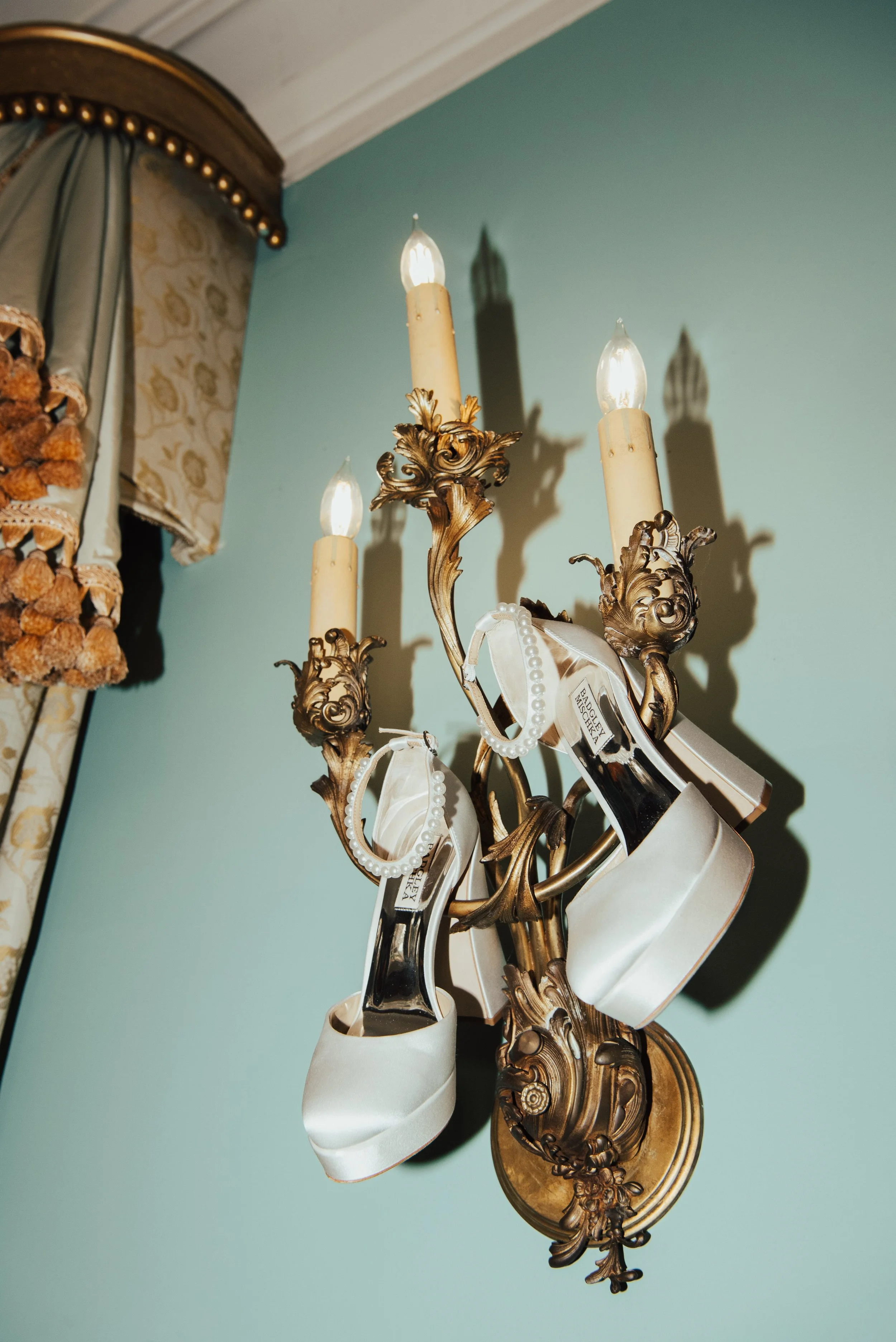 Wedding heels hanging on candelabra on a turquoise wall
