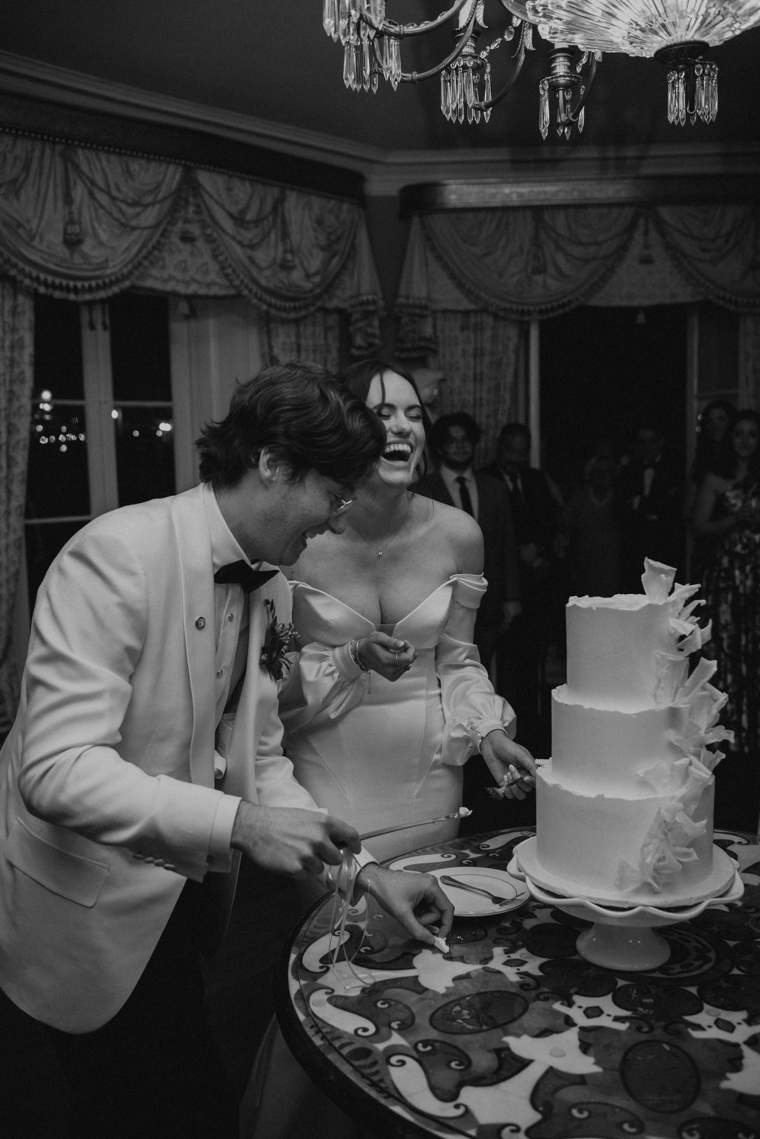Black and white photo of bride and groom laughing as they cut their wedding cake.