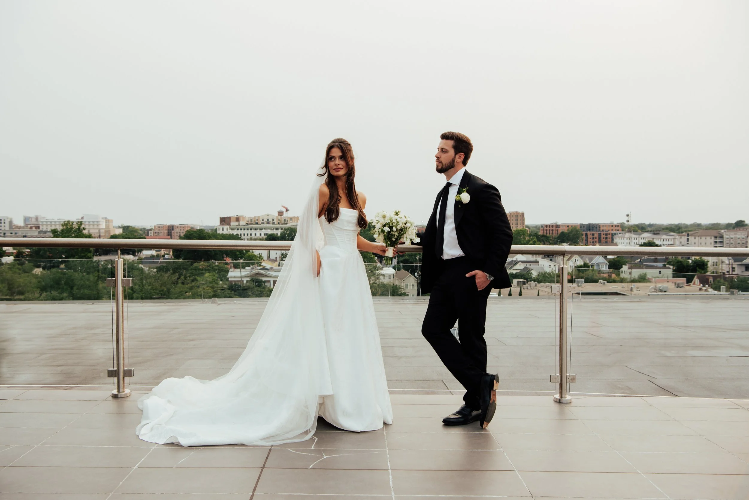landscape photo of bride and groom on a rooftop. Bride is look off to the side as the groom looks at her