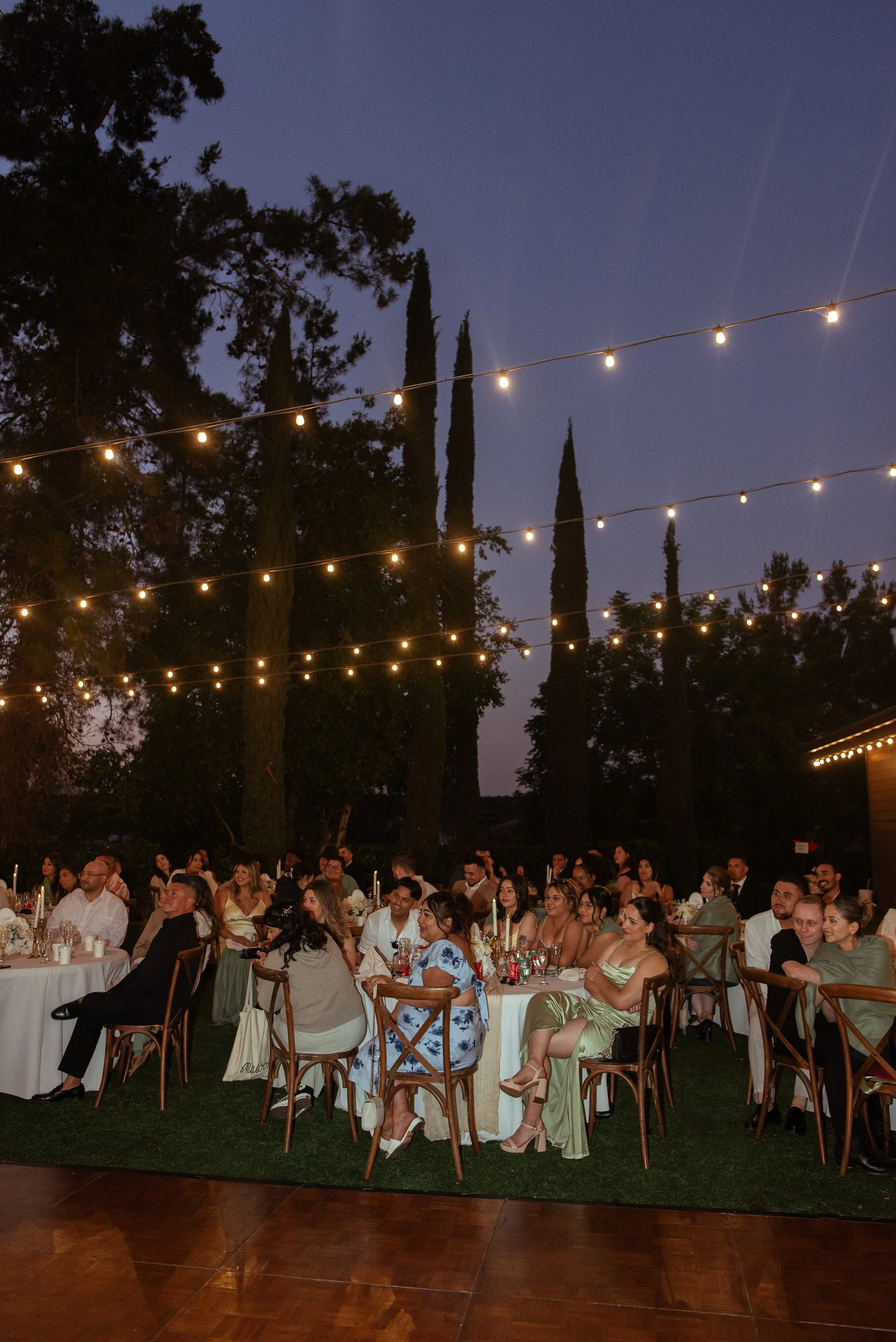 Shot of guest watching the speeches with string light overhead and the sky turning purple.