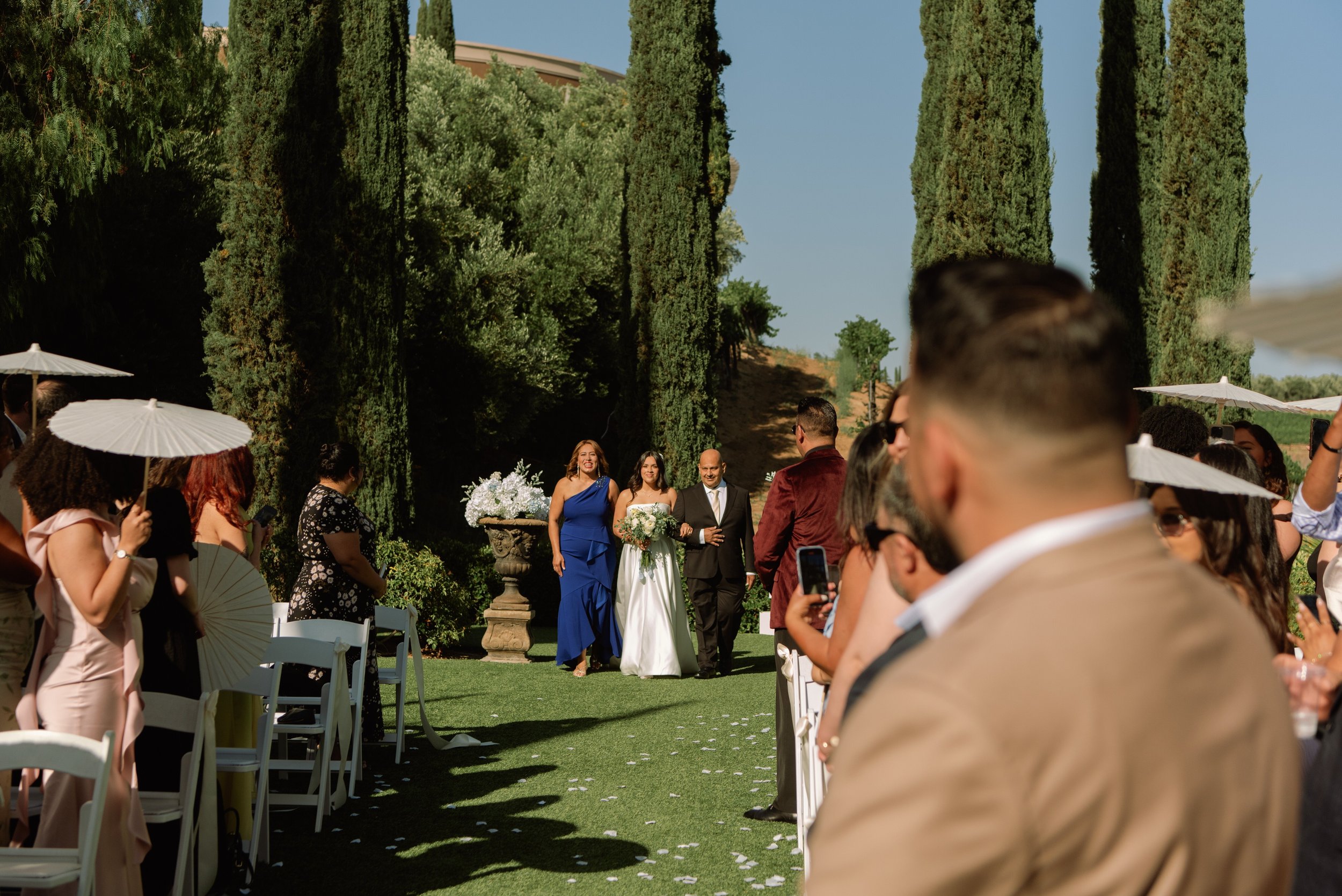A shot looking down the aisle towards the bride and she walks with her parents through the guest.