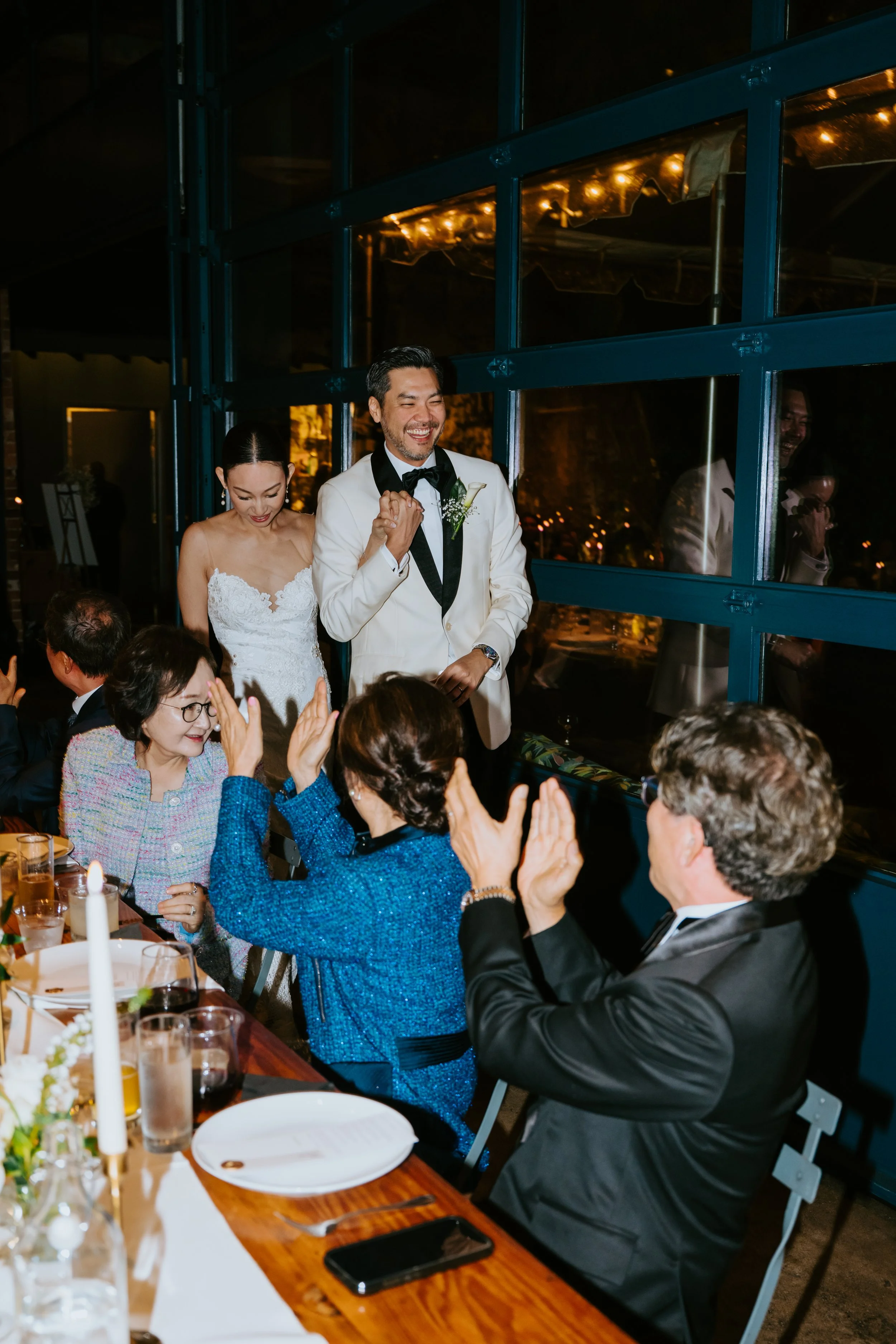 bride and groom walking into their reception holding hands and seated guest clap.