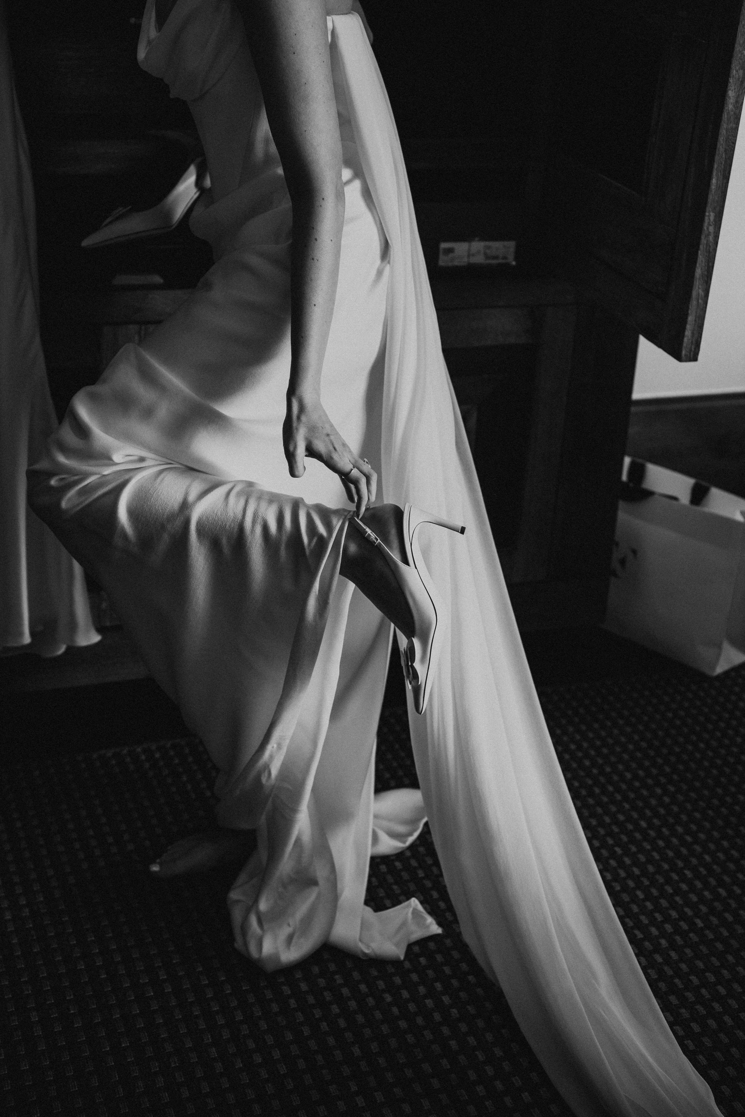 black and white photos of bride pulling on her heel while standing.