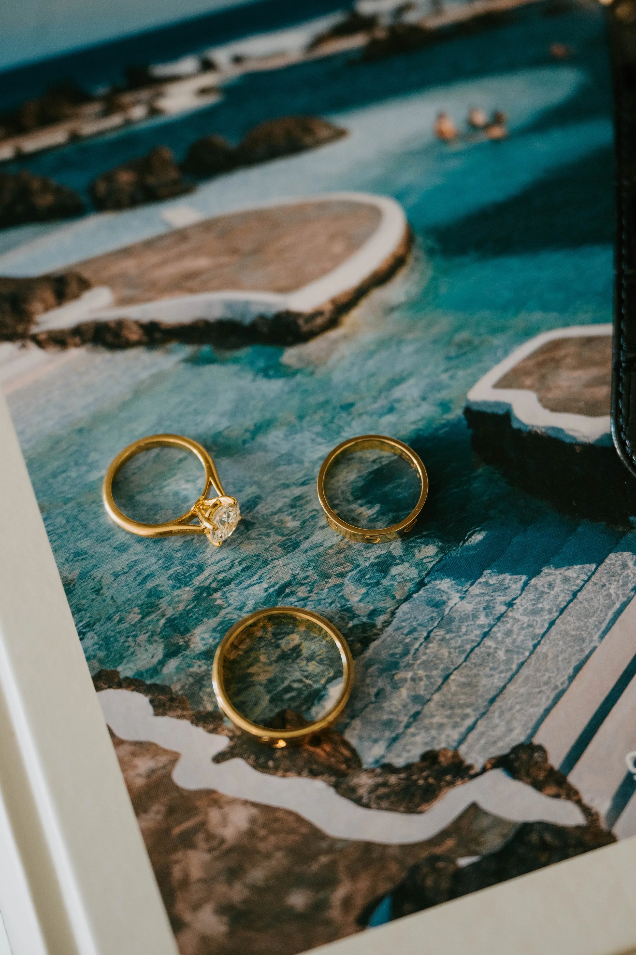 close up photo of engagement and two wedding rings on a book with a picture of a pool on it