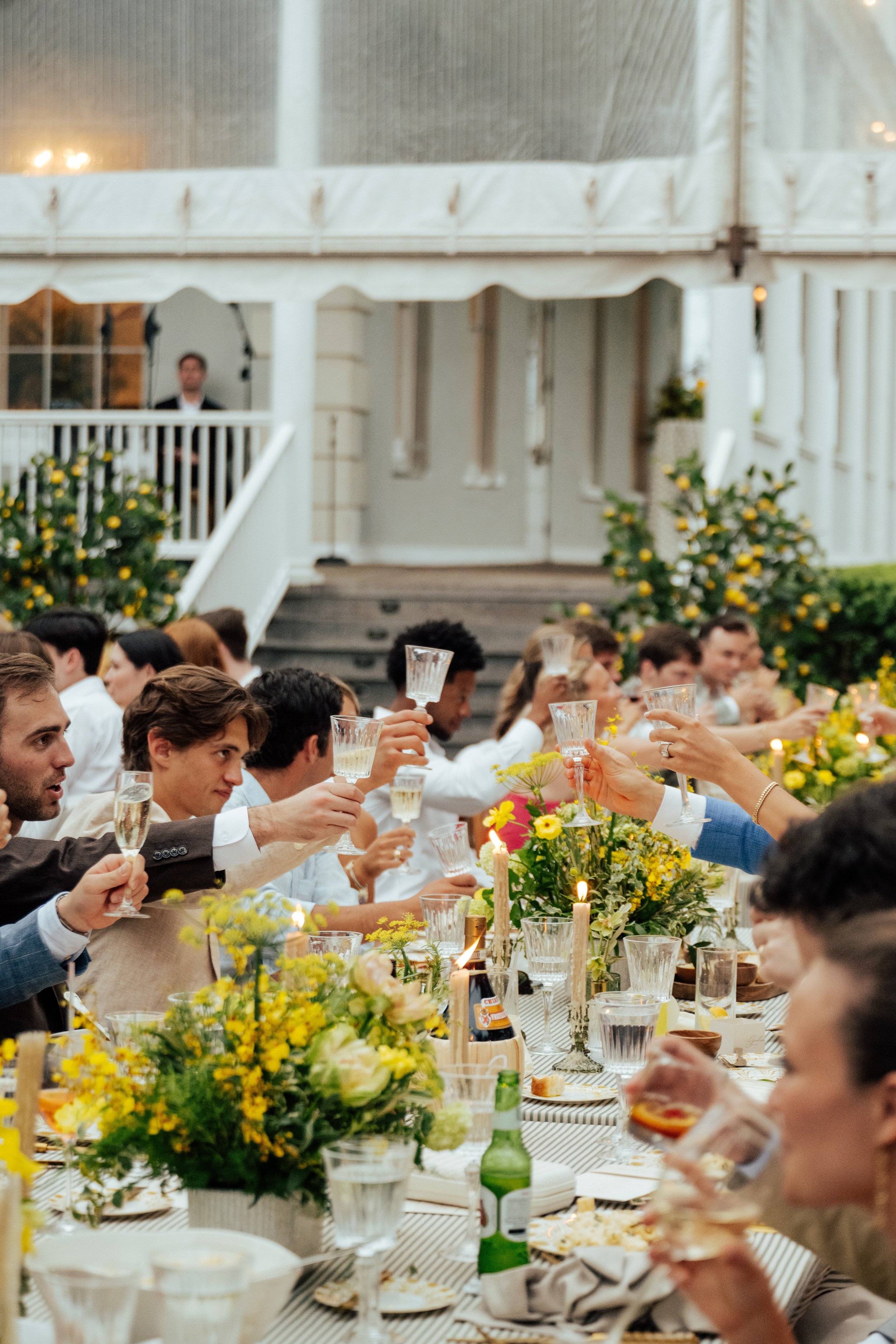 photo of long table with guest on either side holding up their glassed to toast