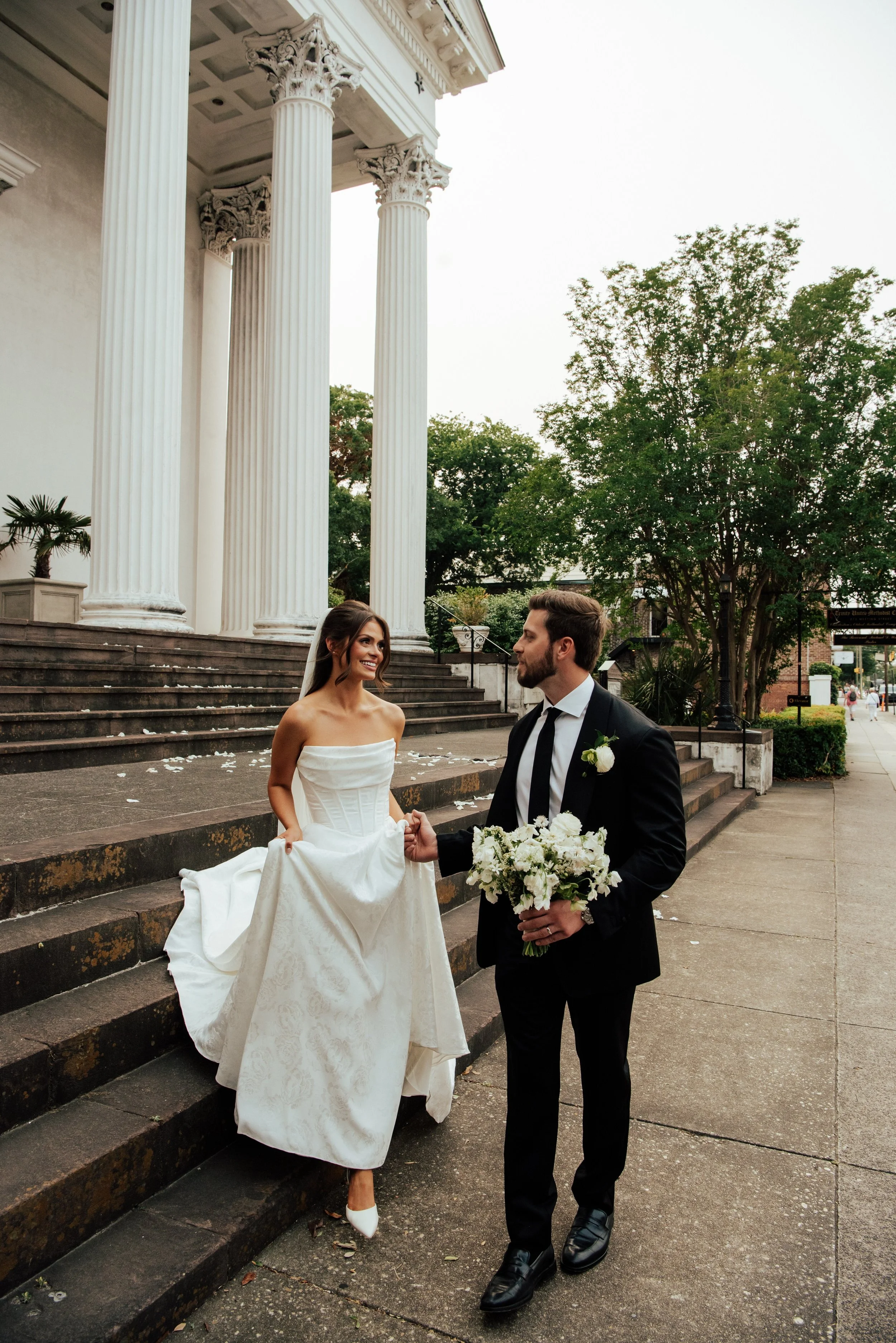 groom helping his bride walk down the stairs of the church entrance.