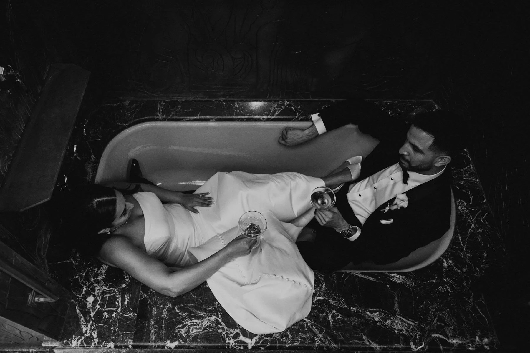 Black and white photo of bride and groom sitting opposite each other holding champagne glasses