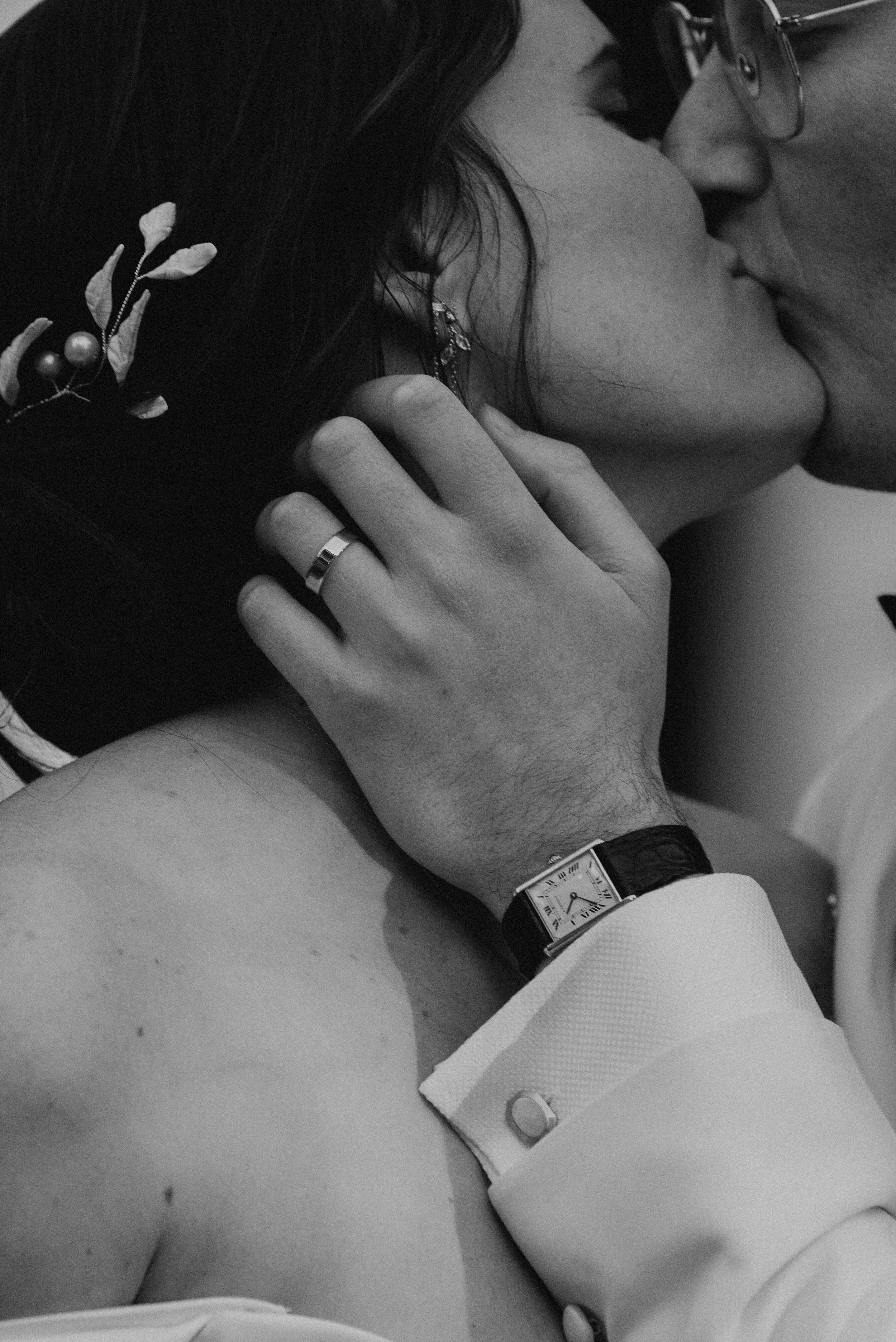 close up of black and white photo of bride and groom kissing. Photo is focus on groom hand with wedding ring holding the brides face.