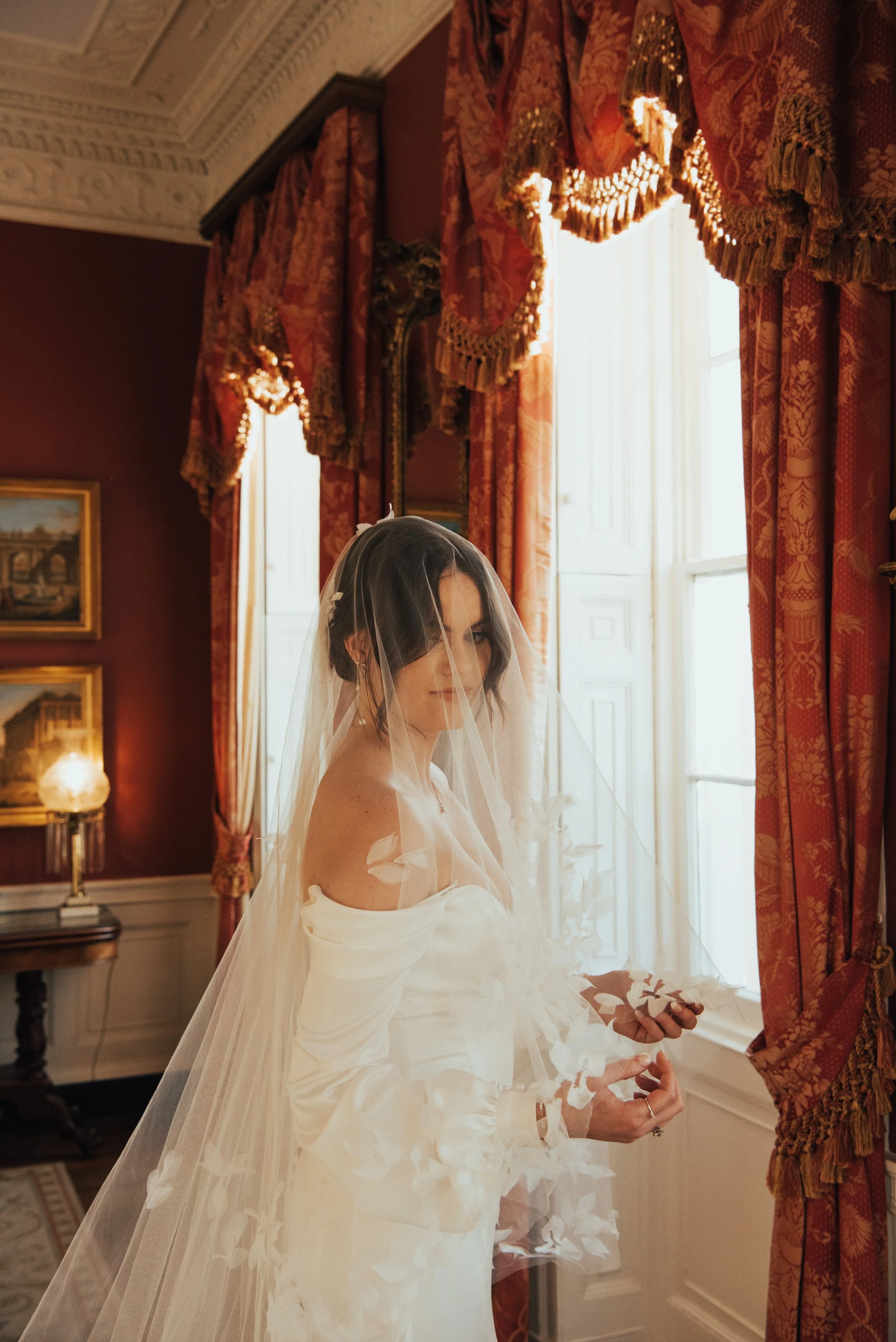 bride standing in front of a window of a red room. She has her veil over her face