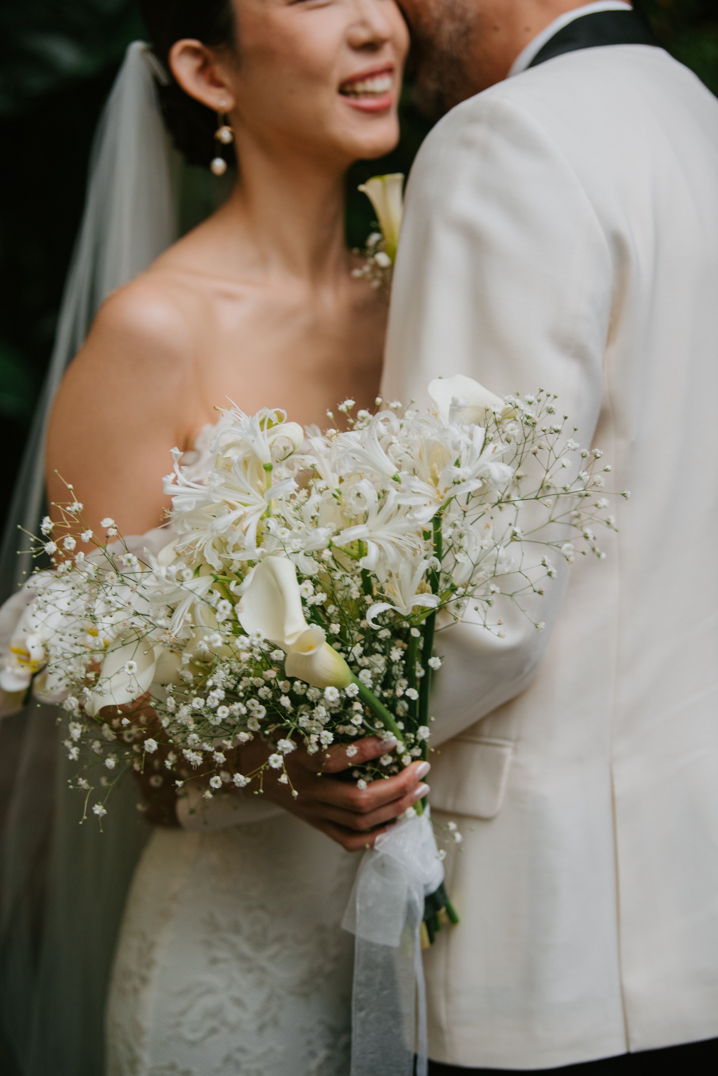 Focus of the photo is on the flowers the bride is holding as groom leans down to whisper in her ear