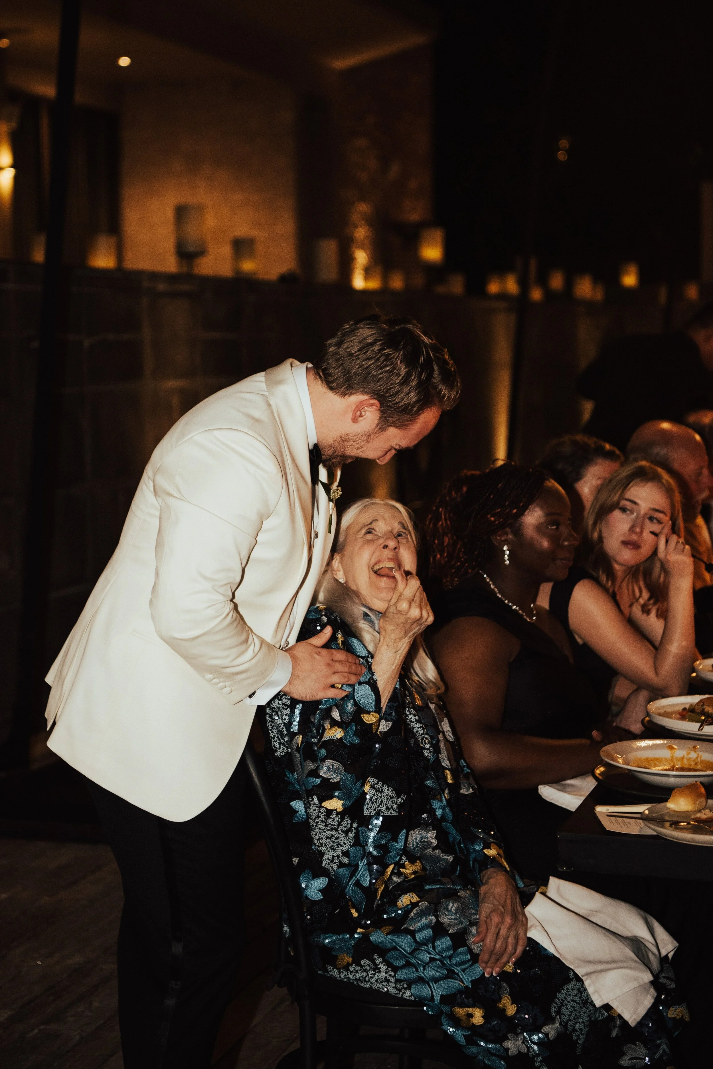 groom standing and making brides grandmother laugh as he smiles down at her