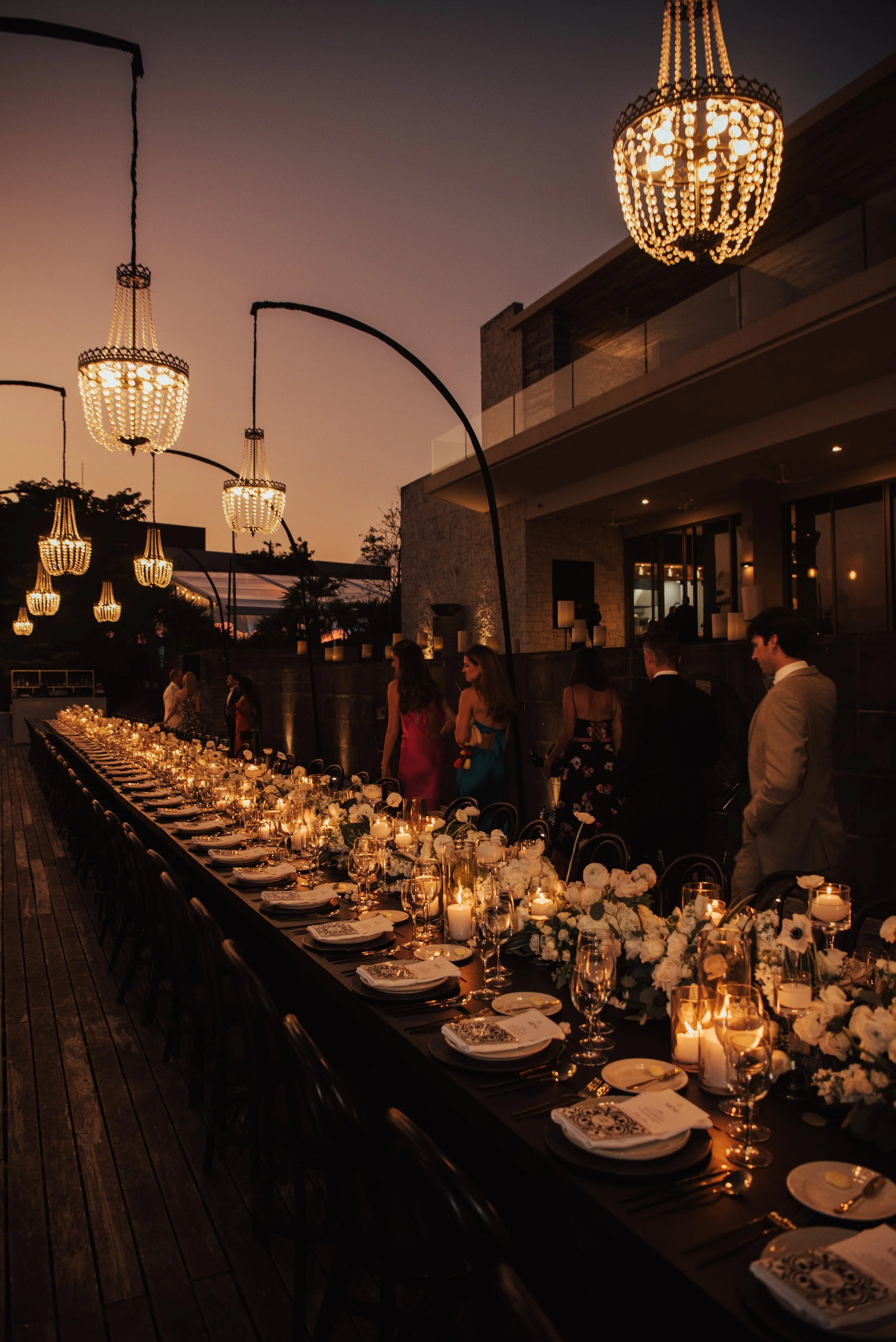 Guest walking along long table at wedding reception with chandeliers hanging over table