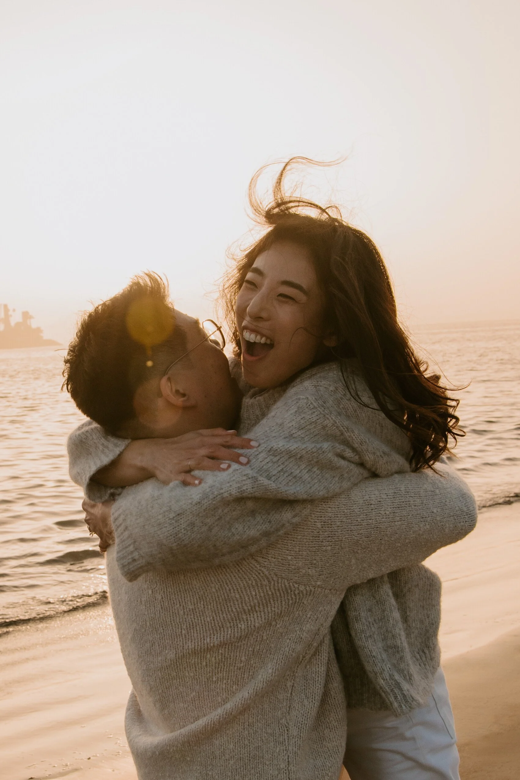Girl laughing as she hugs guy tightly as the sun is setting behind them